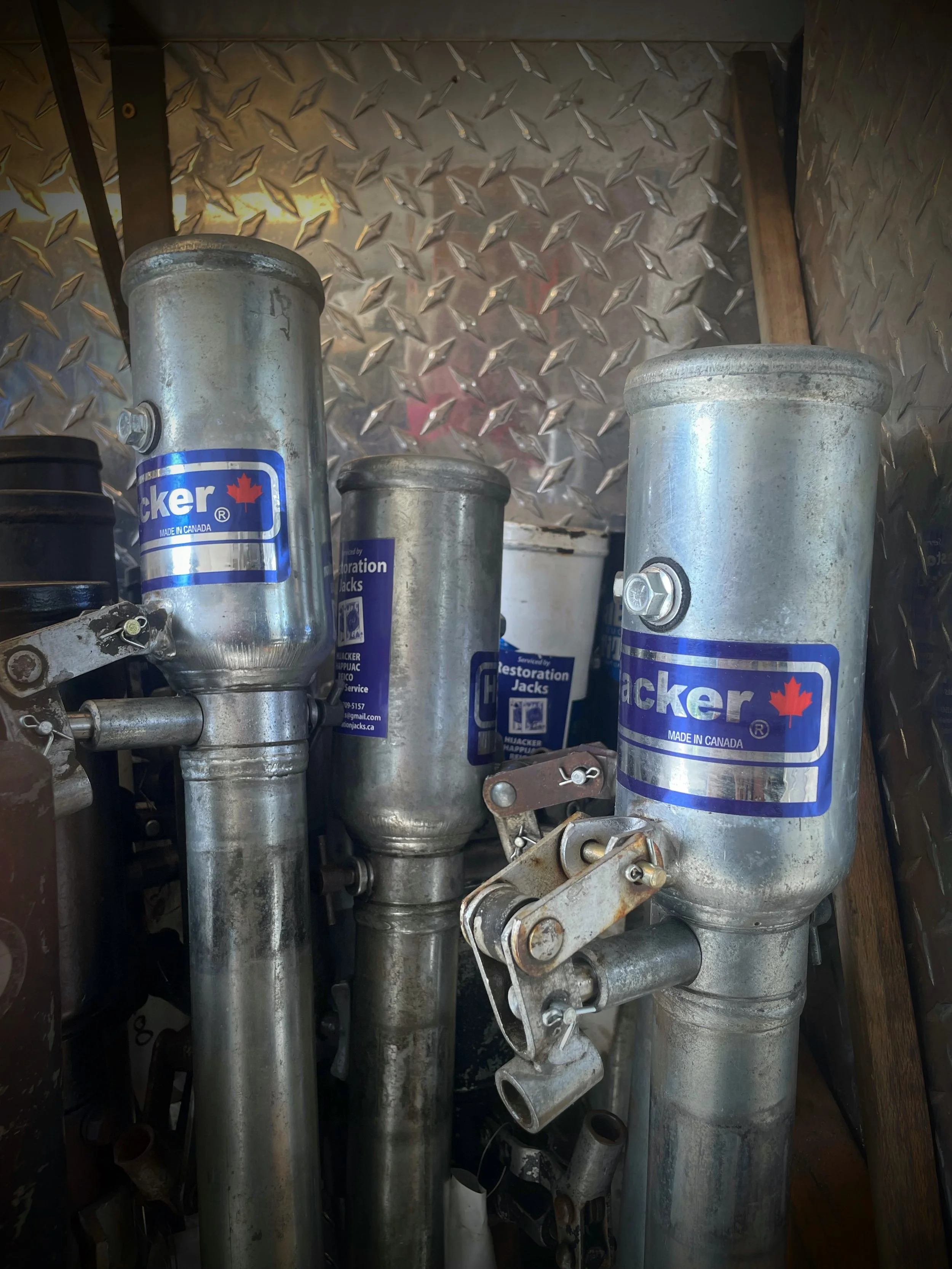 A collection of metal hydraulic camper jacks used to lift a RV or camper off the truck  with blue Hijacker jack labels and fittings, stored vertically inside a room with diamond plate metal walls. in stock reconditioned Jacks ready to use  tested