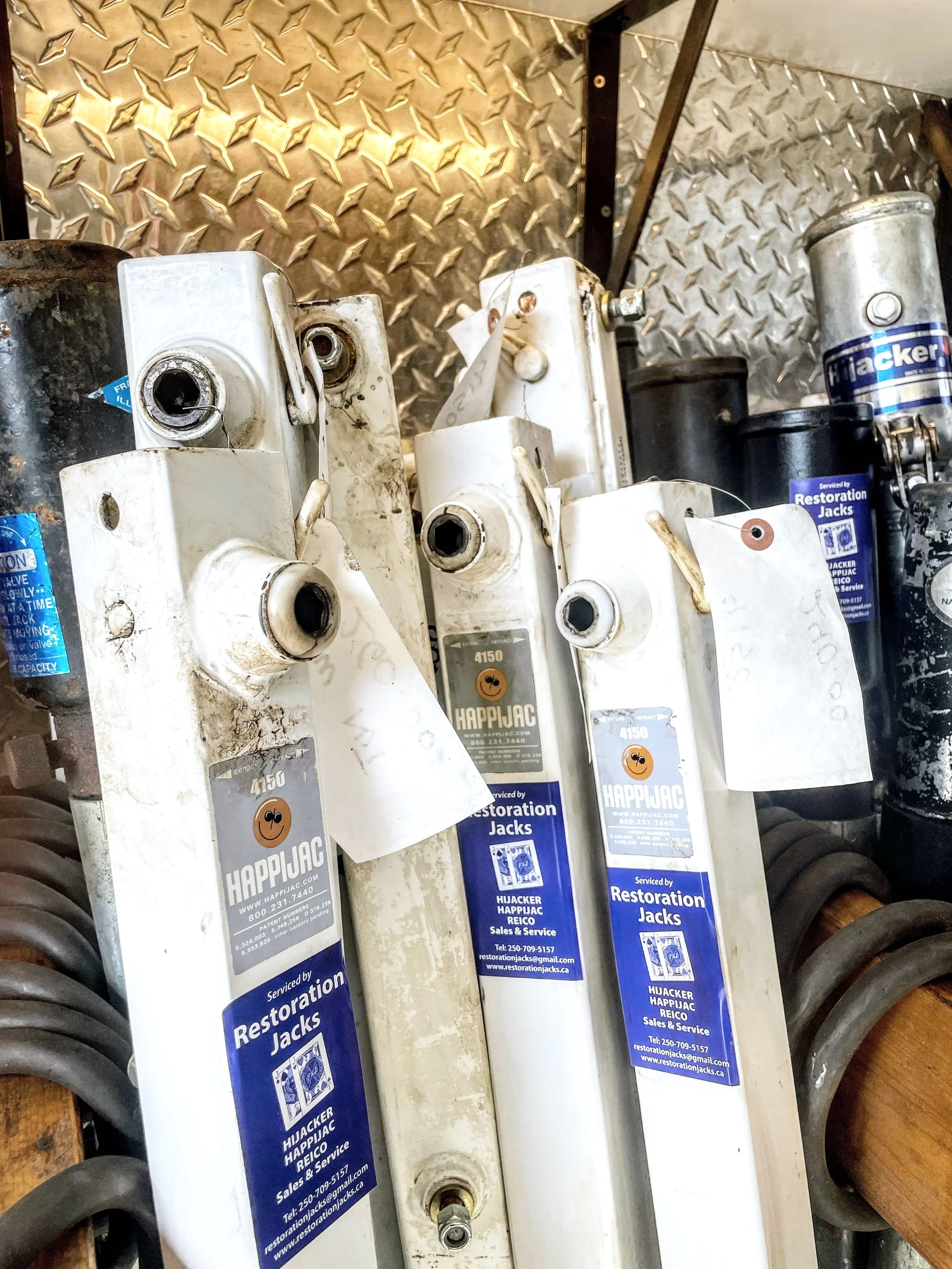 A row of white and black electric jacks  or manual crank  jacks with blue labels from Restoration Jacks, placed on a diamond plate metal surface.