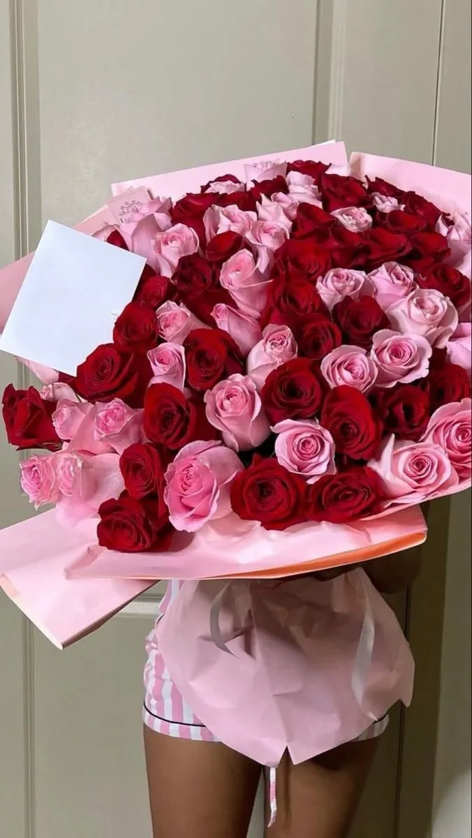 Person holding a large bouquet of pink and red roses wrapped in pink paper.
