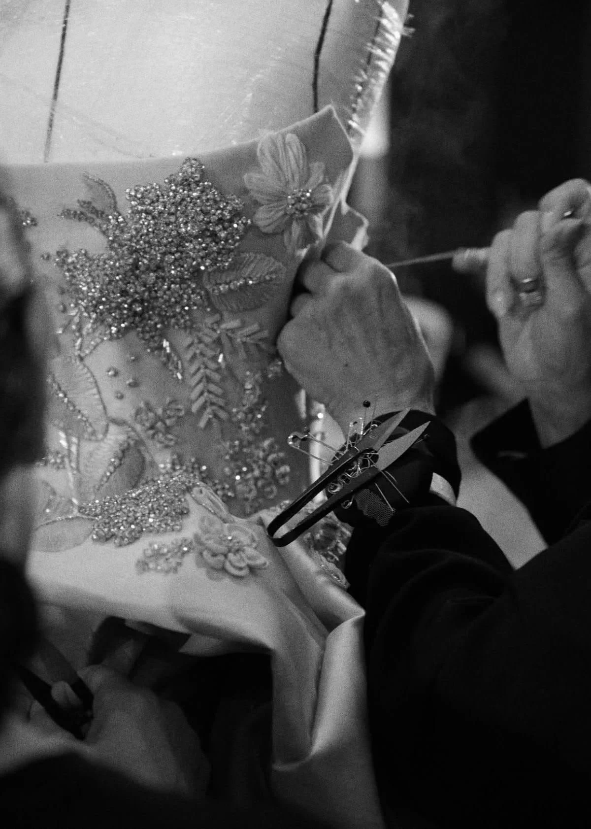 Close-up of hands working on intricate embroidery of floral design with beads and sequins on fabric.