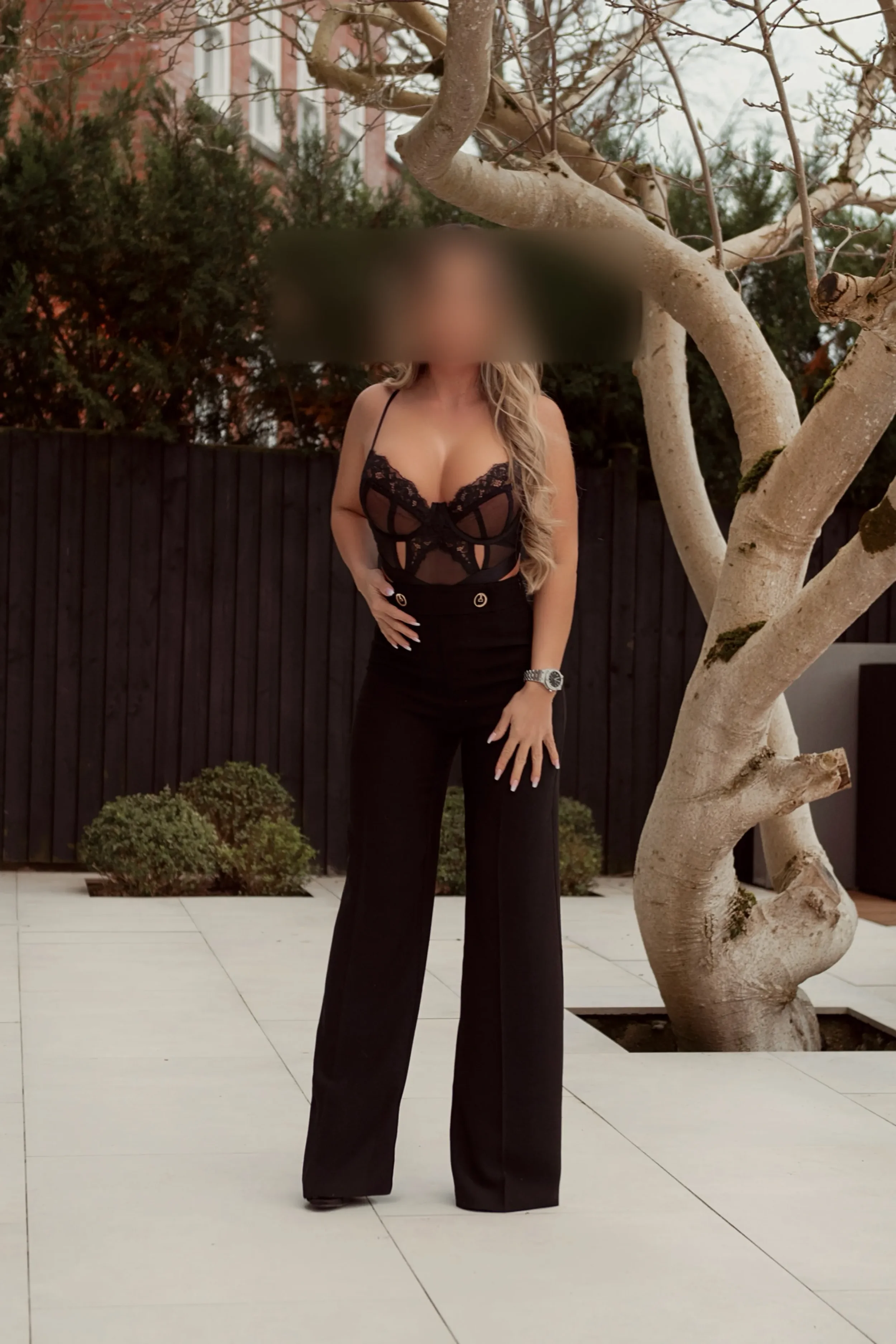 gabriella in black lace top and wide-leg black pants standing outdoors near a leafless tree