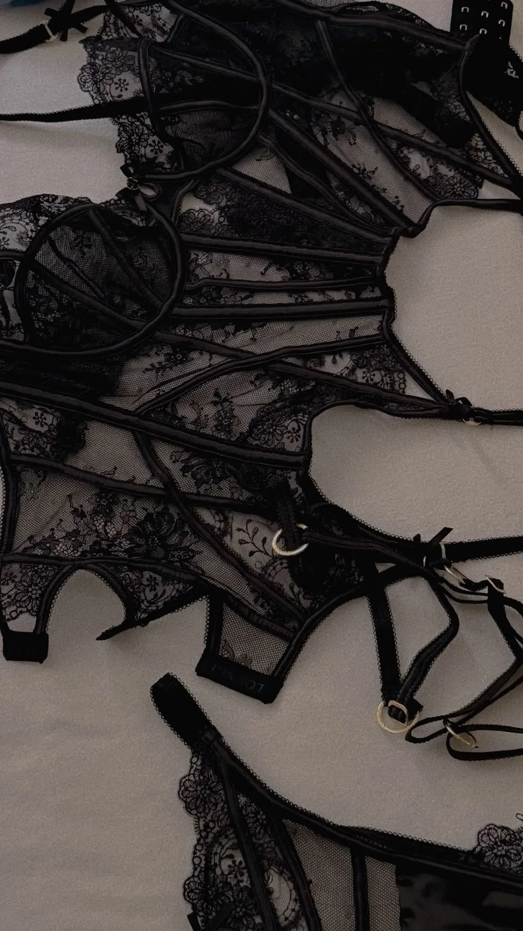 A collection of black lace lingerie with floral patterns and straps, arranged on a light-colored surface.