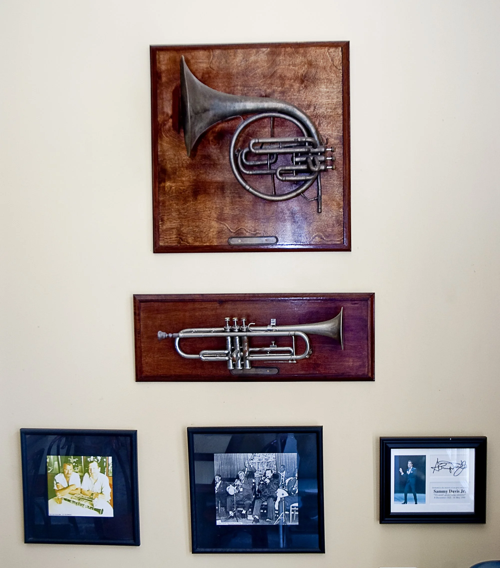 Two brass horns on wooden plaques above three framed pictures on a wall