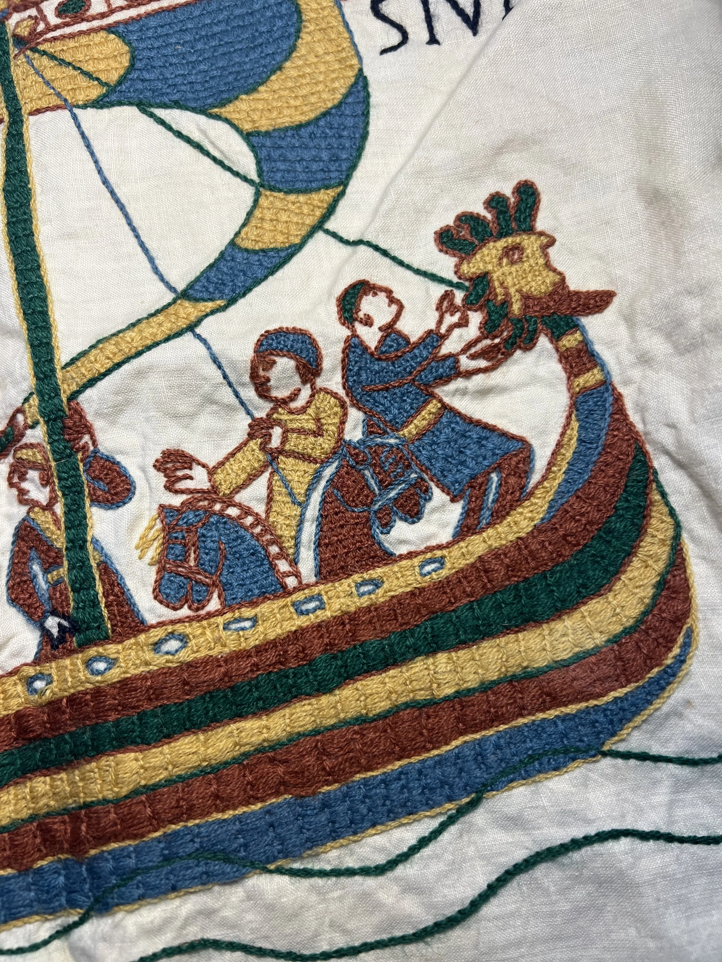 Broderie sur tissu représentant deux enfants dans une barque, avec des couleurs bleu, jaune, vert et rouge.