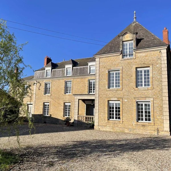 Bâtiment ancien en pierre avec plusieurs fenêtres et un toit en pente, sous un ciel bleu.
