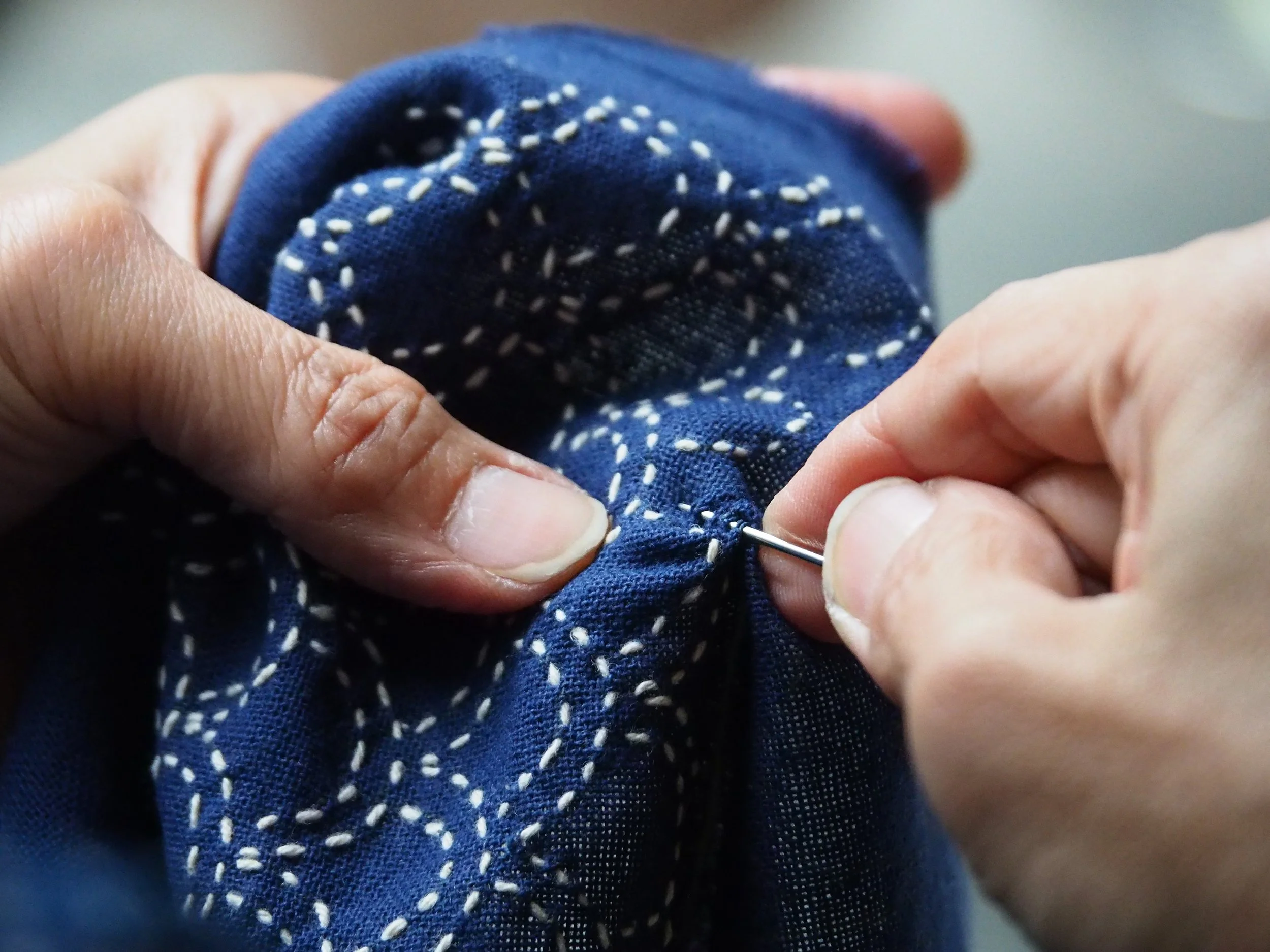 Une personne coud à la main un tissu bleu avec des points blancs.