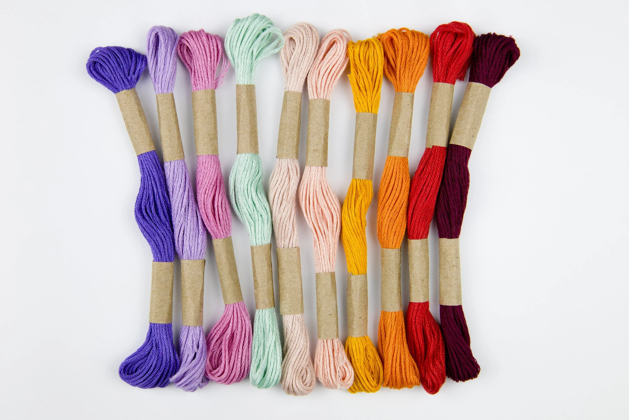 Fils de coton de différentes couleurs disposés en rangée sur un fond blanc.