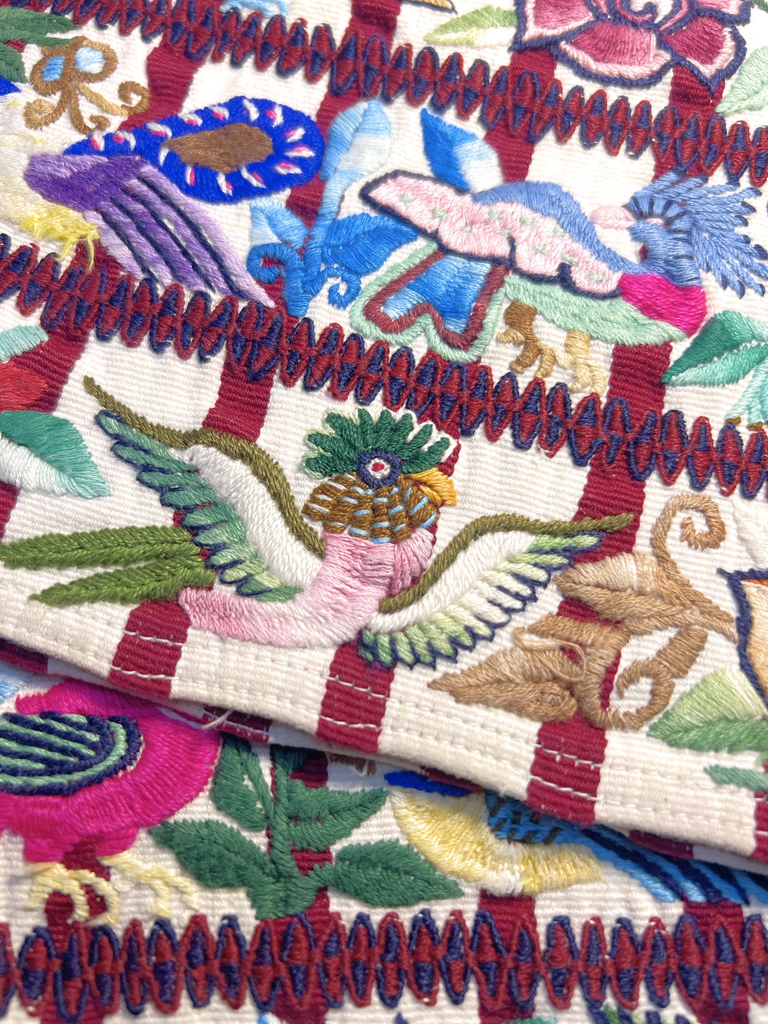 broderie colorée avec des éléments floraux et un oiseau de profil, sur fond de motifs géométriques rouge et blanc