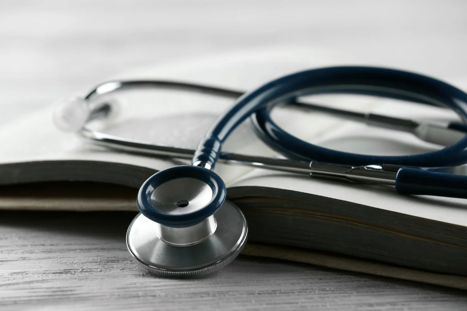 A stethoscope resting on a medical book or journal, on a white wooden surface.