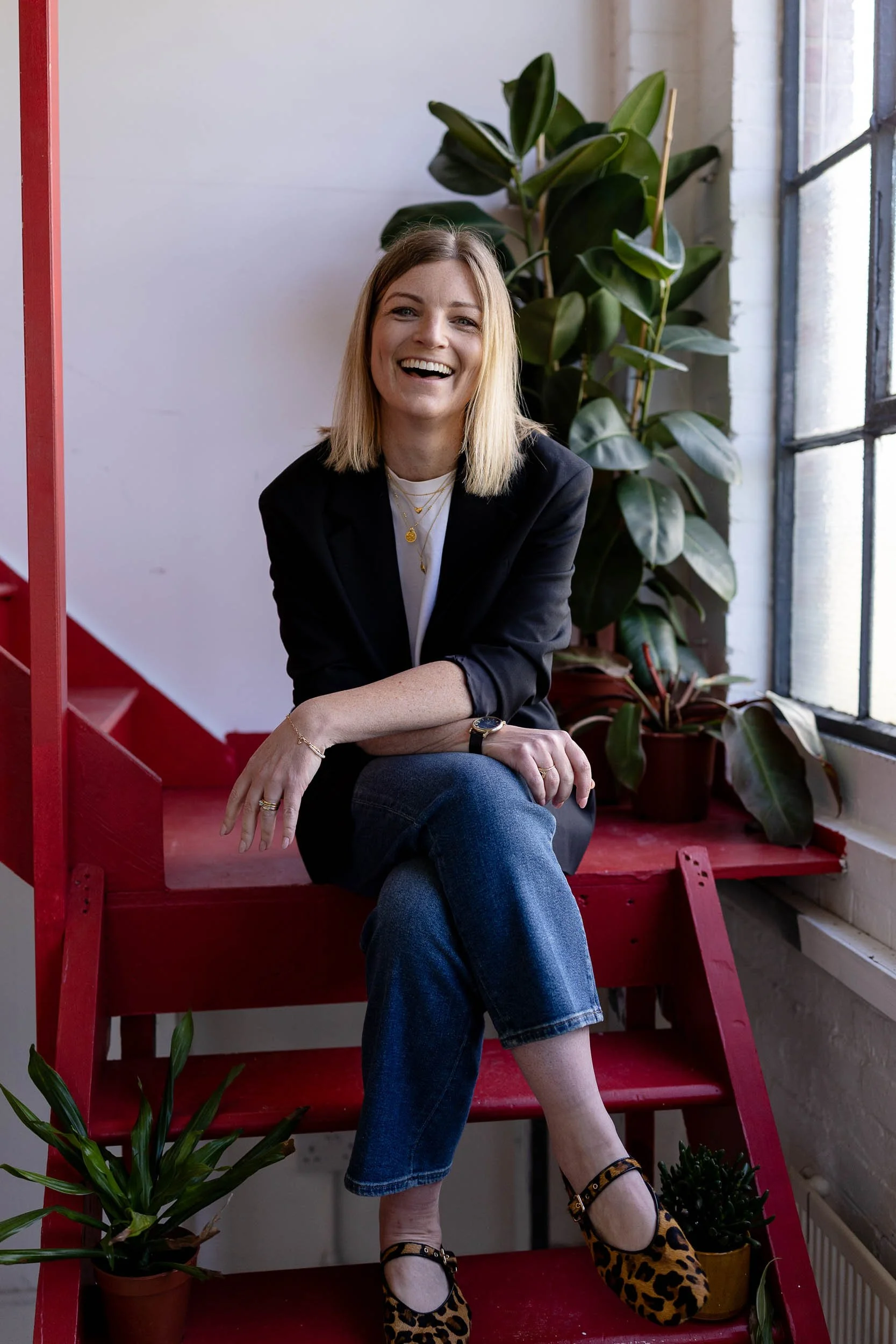 Retail merchandising consultant sitting in red steps with legs crossed smiling at camera