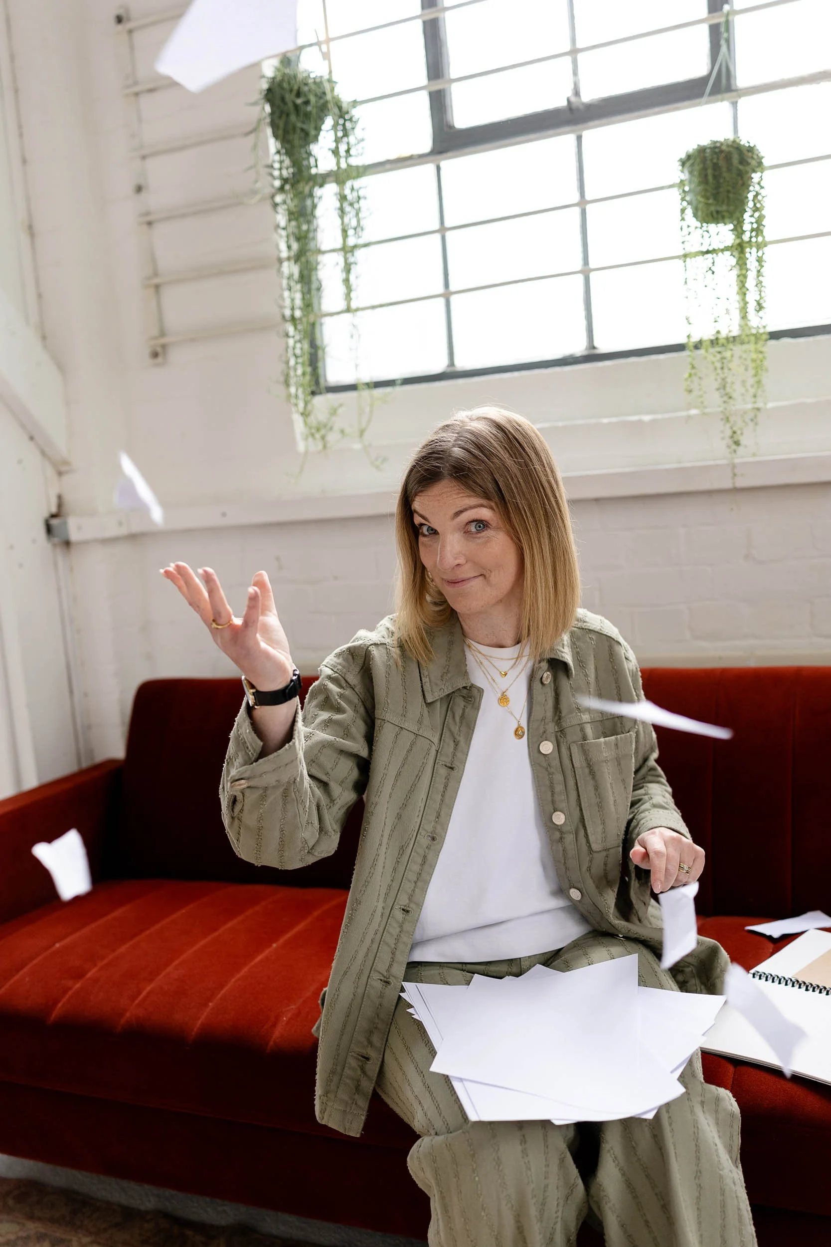 Fashion merchandising expert sat on red sofa throwing paper into air