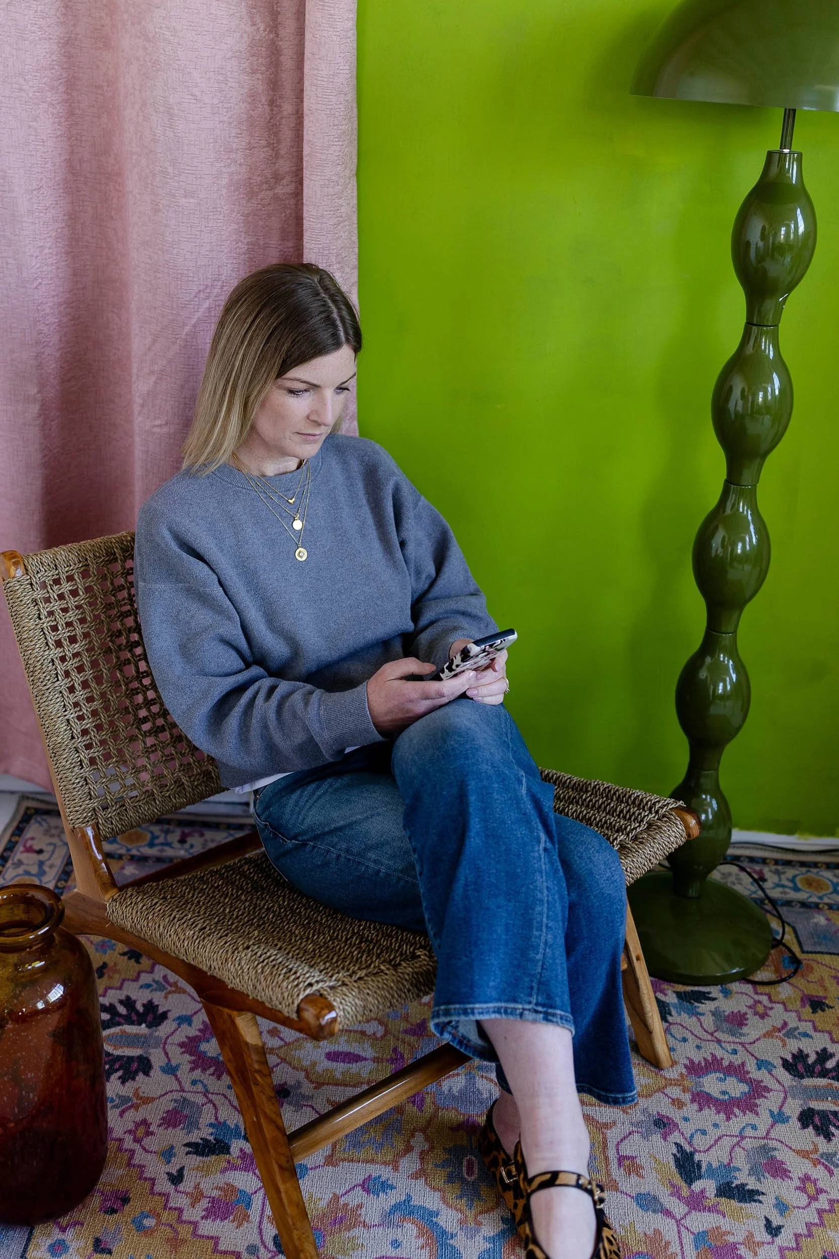 Merchandising consultant sat on wicker chair in bright studio looking at phone