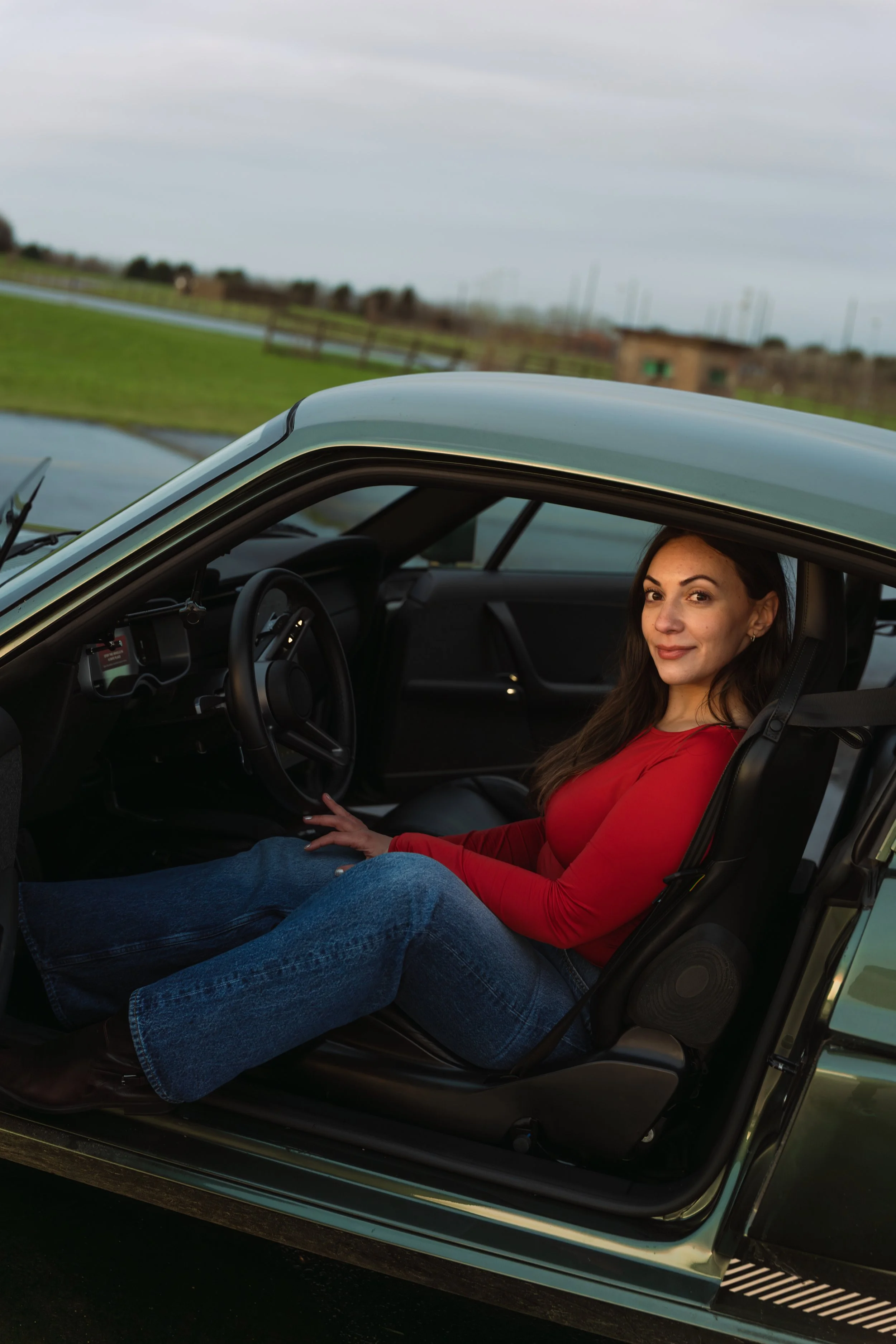 Young woman resting in the driver’s seat of a vintage car, with a scenic outdoor background.