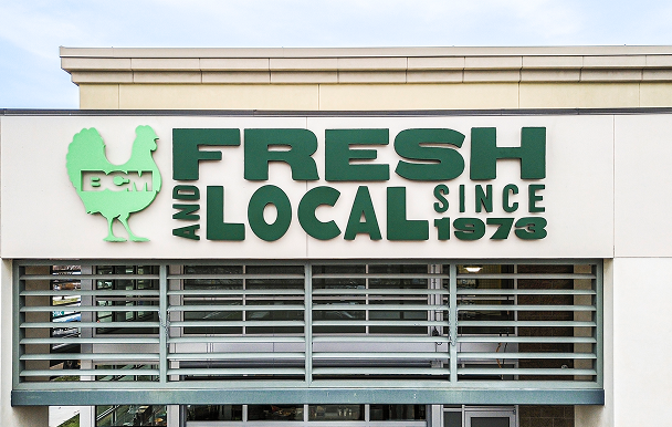 Sign on building reading 'Fresh and Local Since 1973' with a green chicken logo containing the initials 'BCM'.
