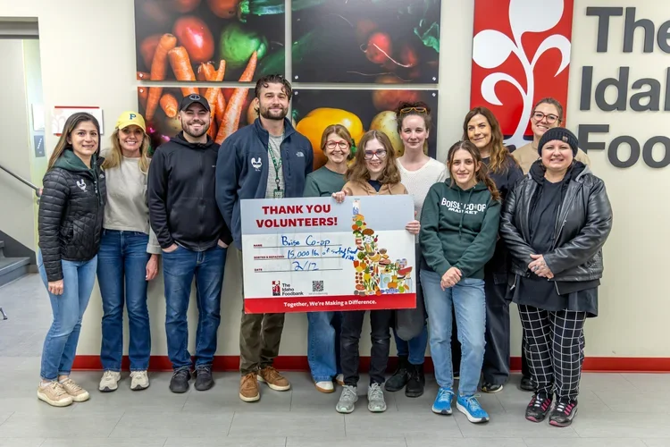 Group of ten volunteers standing inside a grocery store, holding a large check for $15,000 made out to Boise Co+op, with a display of vegetables on the wall behind them.