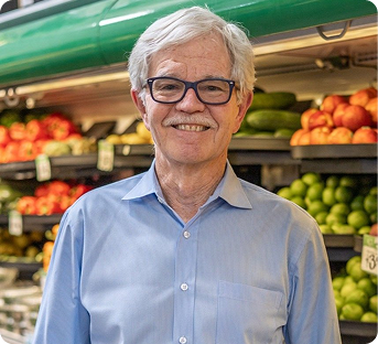 Smiling elderly man with gray hair and glasses shopping for produce at a grocery store.