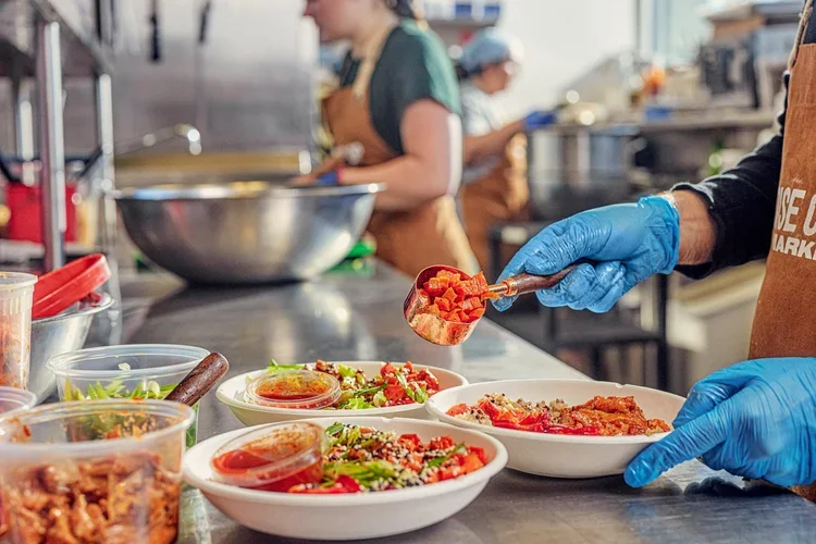 A person wearing blue gloves preparing bowls of food in a commercial kitchen.