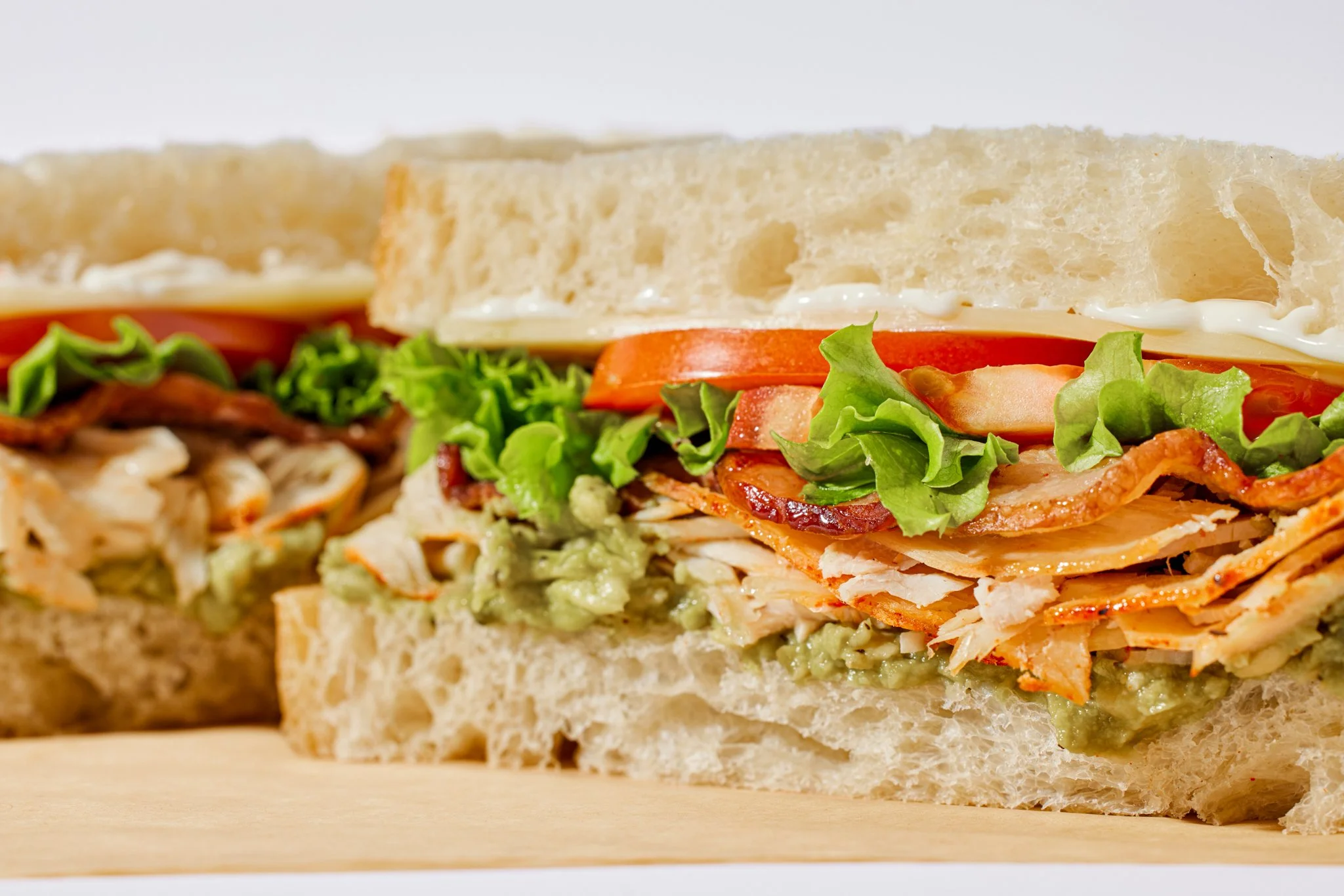 Close-up of a sandwich with bread, lettuce, tomato, bacon, turkey, cheese, and mayonnaise.