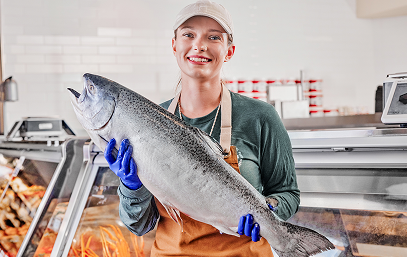 Smiling worker holding a large fish in a seafood market or fish shop.
