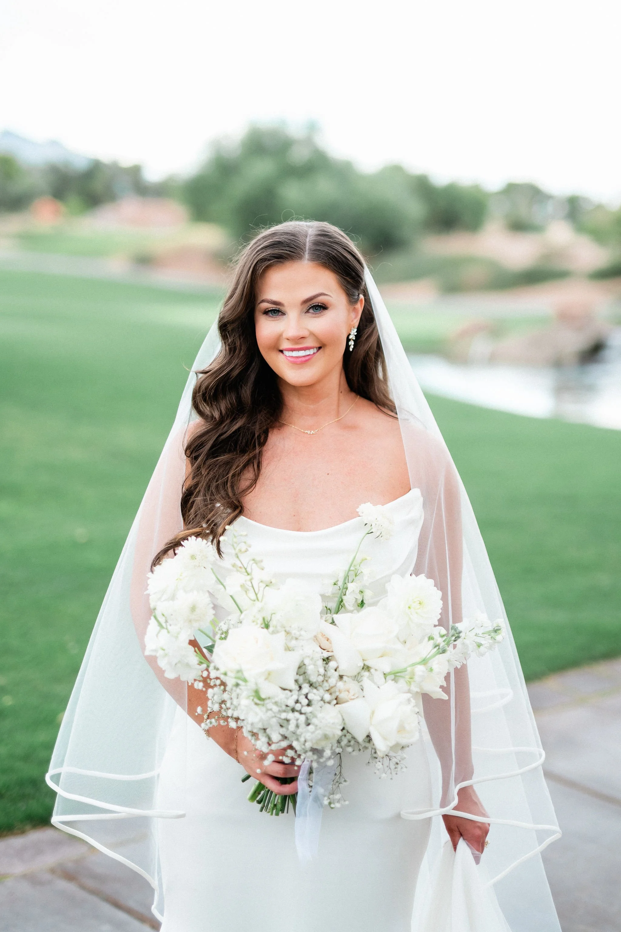 Bridal portrait of smiling bride with veil and white bouquet at Canyon Gate Country Club Las Vegas, hair and makeup by Marai A for Amelia C & Co, photography by Kristen Marie Weddings