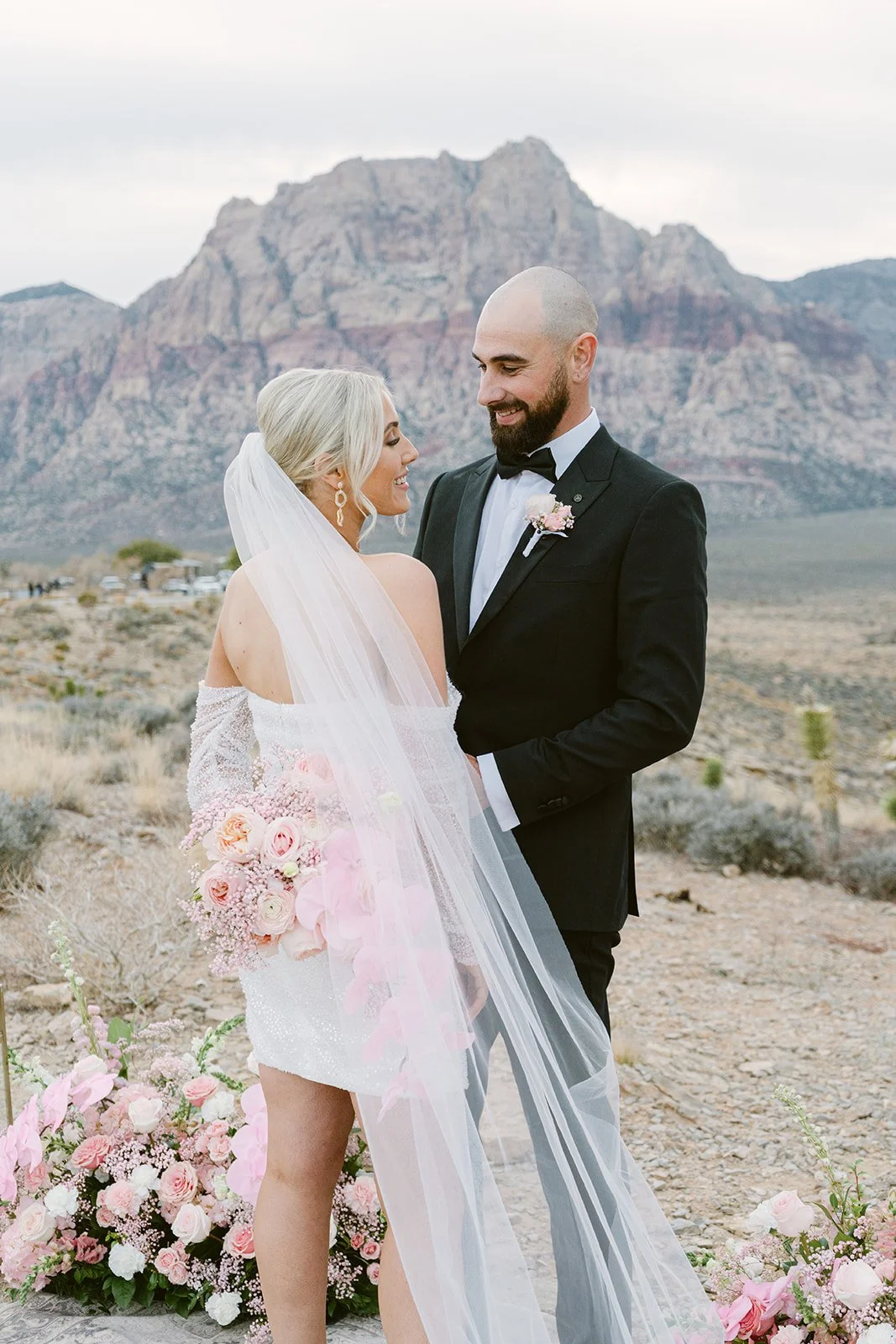 Bride with flowing veil and pink bouquet at Red Rock Canyon Las Vegas desert elopement, hair and makeup by Luci L for Amelia C & Co, photography by Kristen Joy
