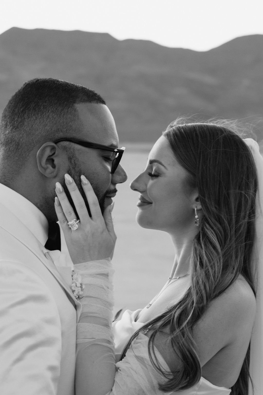 Close-up black and white portrait of Cameron and Bruce forehead to forehead at Dry Lake Bed Las Vegas elopement, engagement ring detail, hair and makeup by Marai for Amelia C & Co, photography by Sofia Teresa