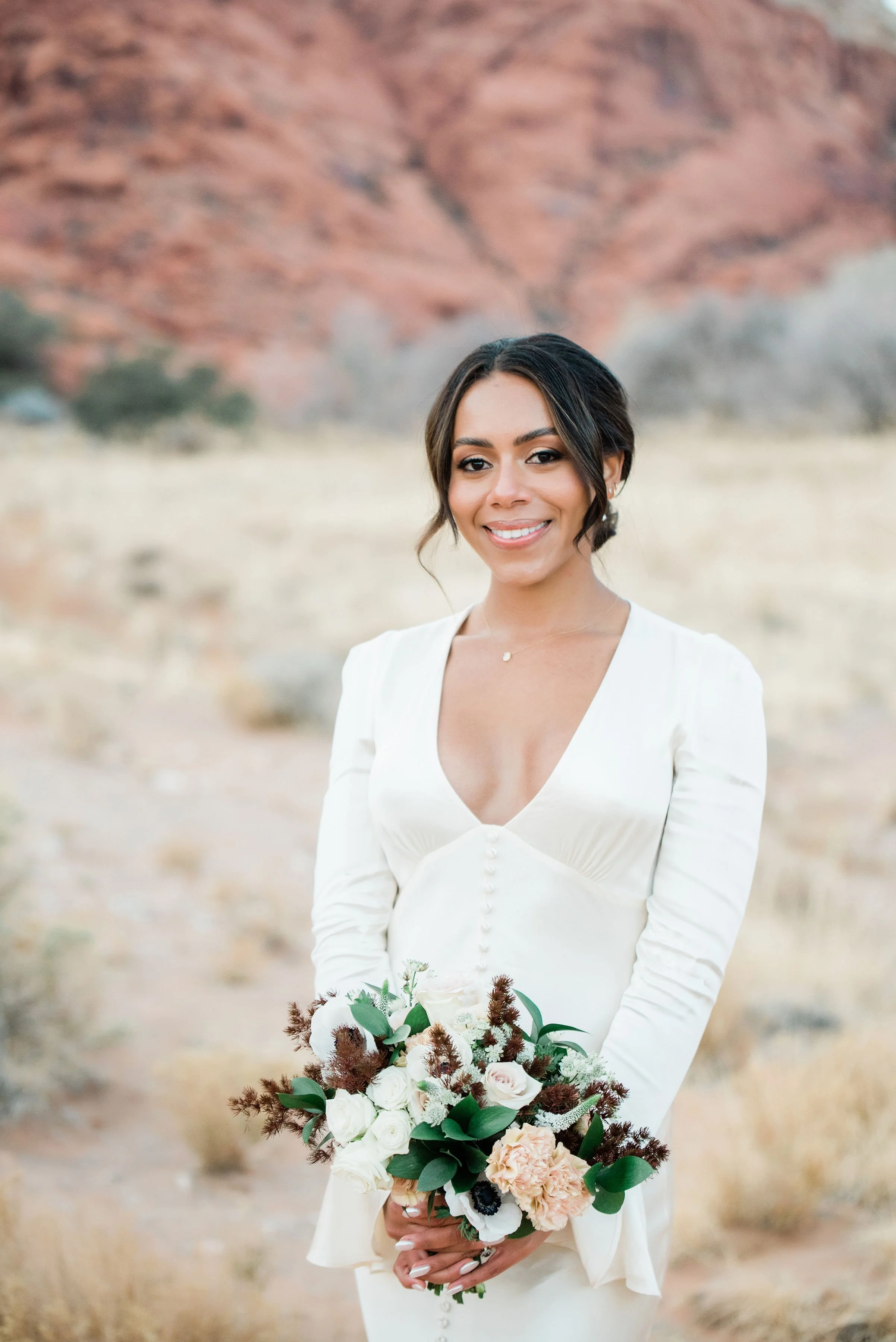 Bridal portrait of Martinique smiling with bouquet at Red Rock Canyon elopement, hair and makeup by Luci for Amelia C & Co, photography by Cactus Collective Weddings