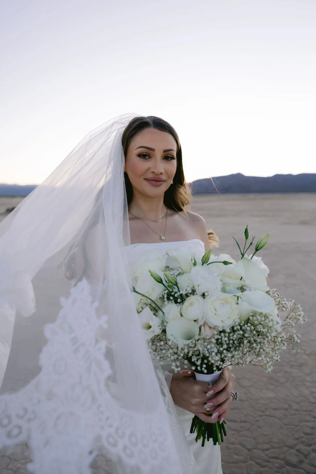  Bridal portrait of Cameron in lace off-shoulder gown with veil and white bouquet at Dry Lake Bed Las Vegas elopement at dusk, hair and makeup by Marai for Amelia C & Co, photography by Sofia Teresa