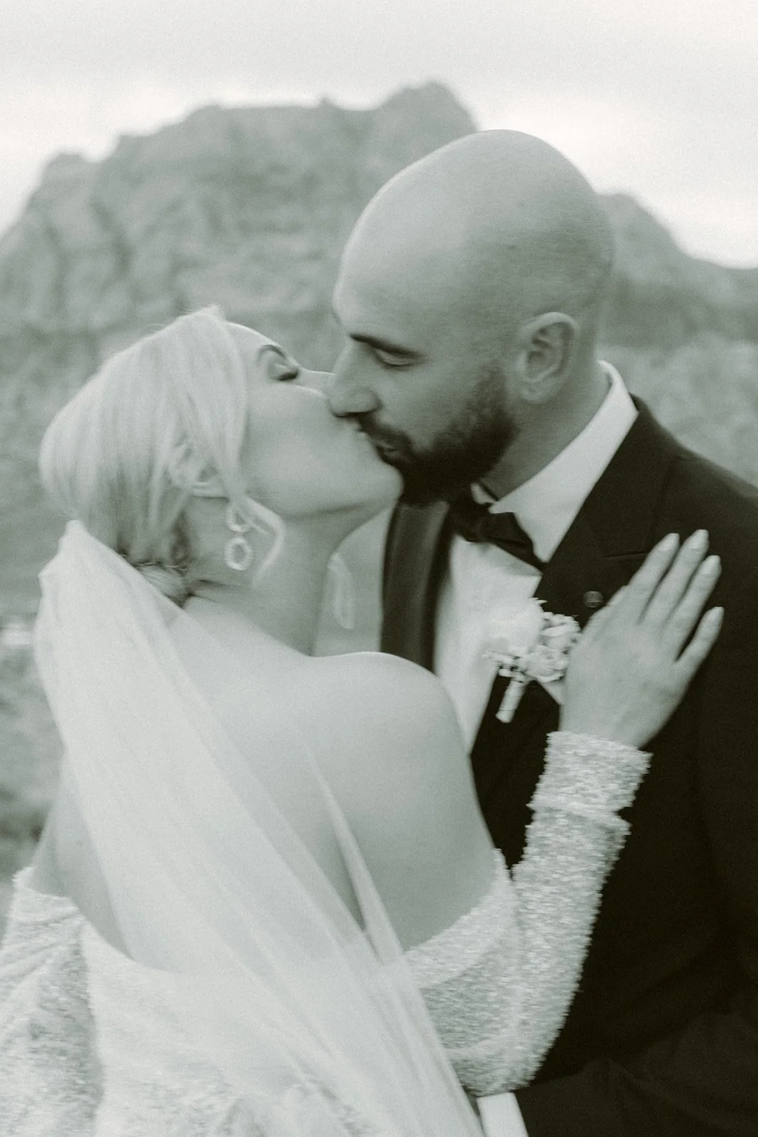 Black and white film style bridal portrait at Red Rock Canyon Las Vegas elopement, bride laughing with bouquet and desert mountain backdrop, hair and makeup by Luci L for Amelia C & Co, photography by Kristen Joy