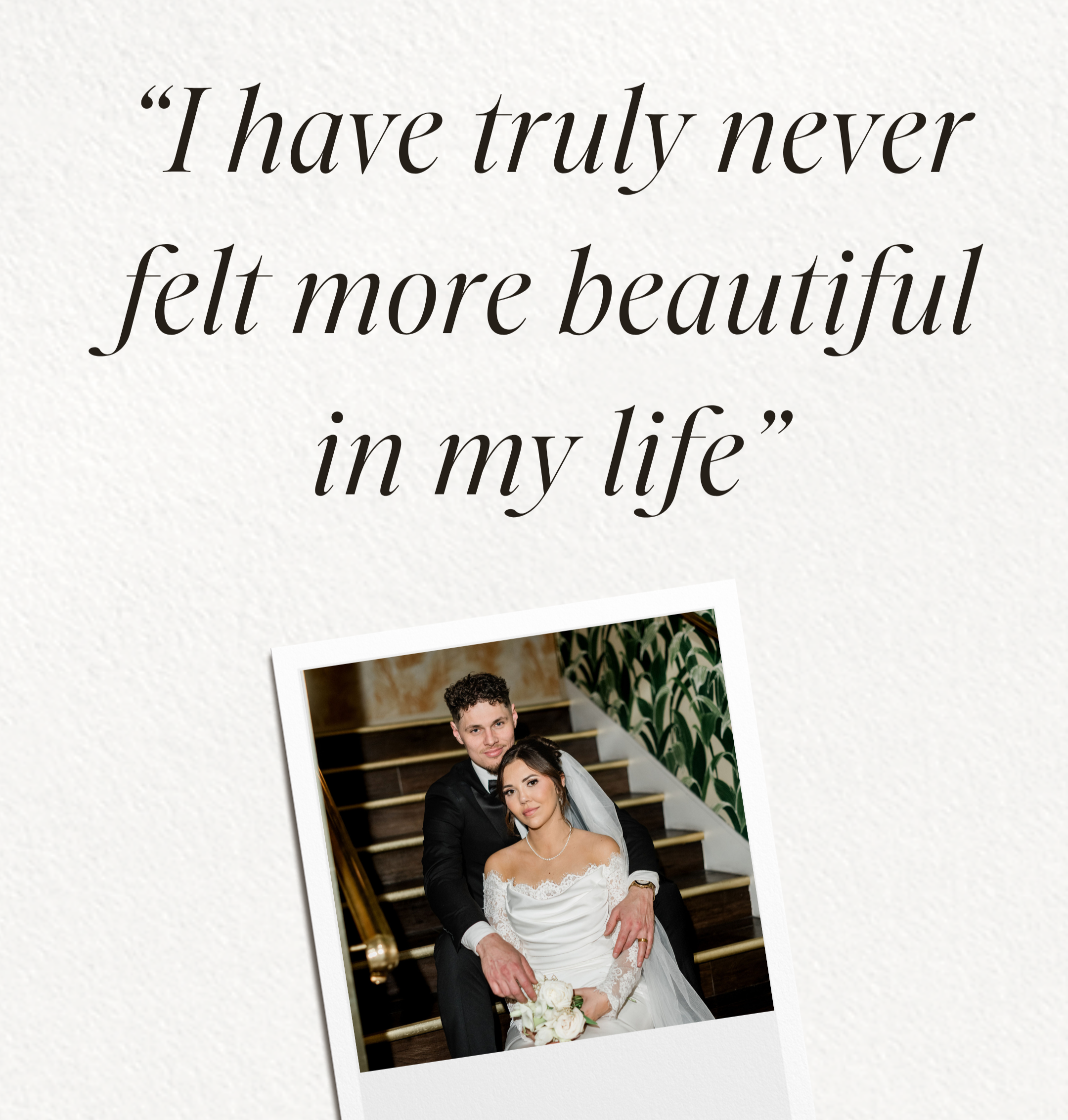 A wedding photo of a couple dressed in formal wedding attire. The groom is in a black tuxedo and the bride is in a white lace wedding dress holding a bouquet of white roses. They are standing on a staircase with gold banisters, smiling.