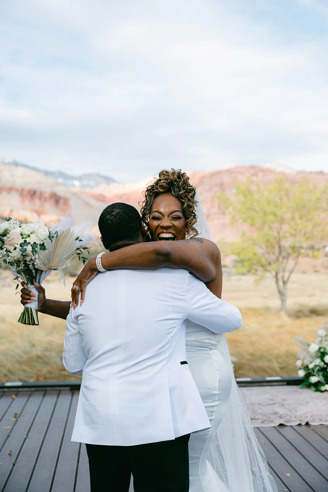 Aretha beaming over Jaxon's shoulder during first look embrace at Red Spring Boardwalk Las Vegas elopement, hair by Courtney and makeup by Natalia for Amelia C & Co, photography by Desert Wildflower