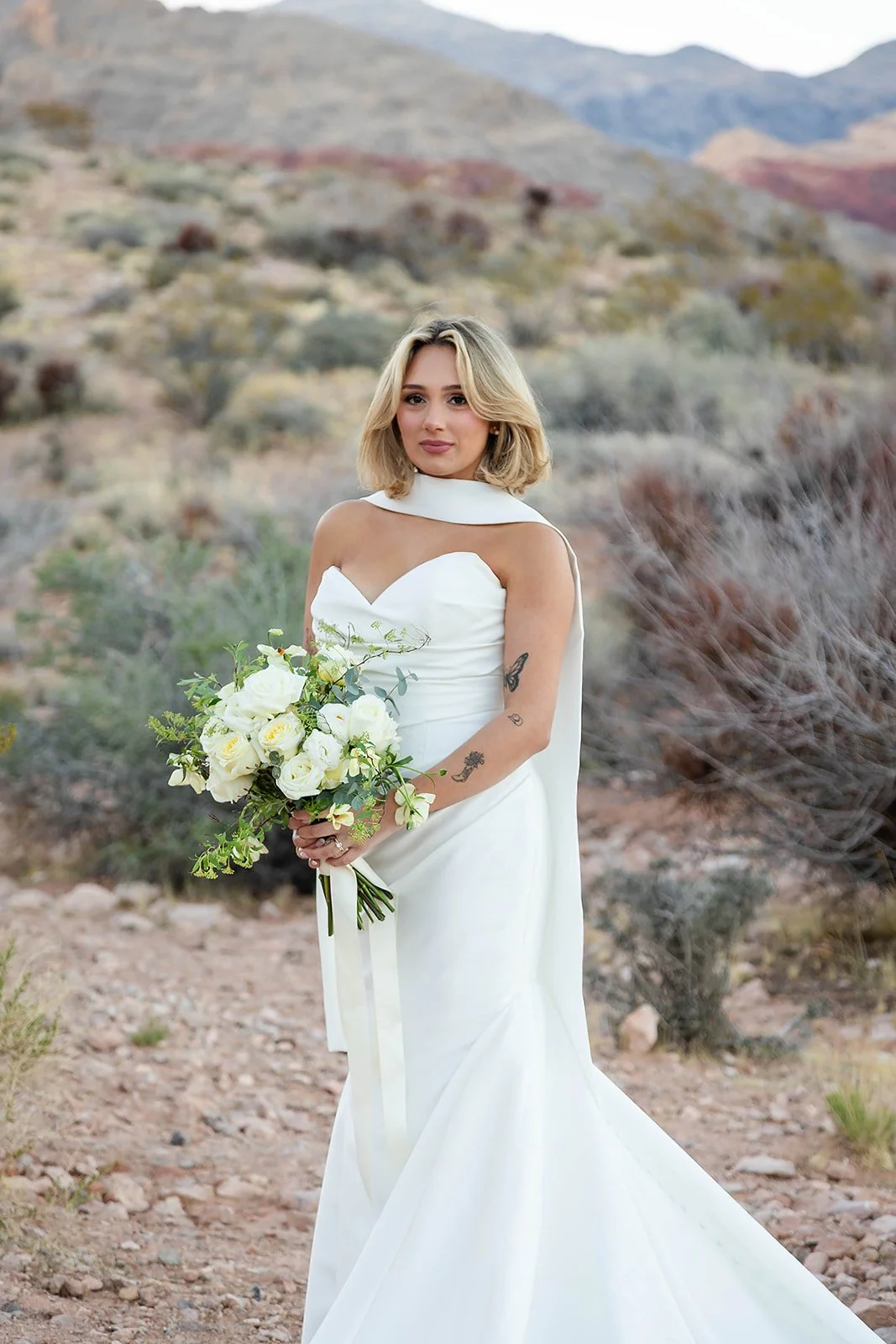 Bridal portrait of Melysa in cape halter gown with train and white bouquet at Red Spring Boardwalk Las Vegas elopement, hair by Luci and makeup by Natalia for Amelia C & Co, photography by Onyx & Arrow