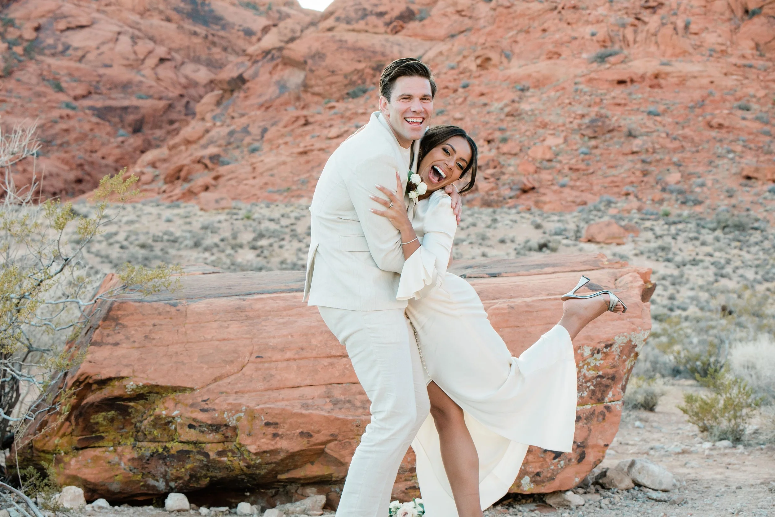 Martinique and James laughing with joyful leg kick at Red Rock Canyon elopement, hair and makeup by Luci for Amelia C & Co, photography by Cactus Collective Weddings