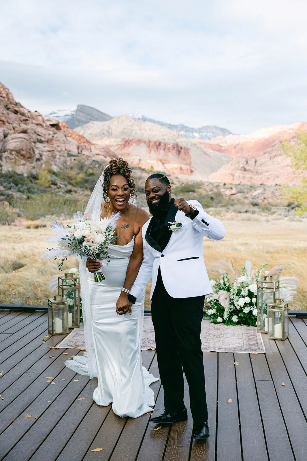 Aretha and Jaxon celebrating just married on ceremony deck at Red Spring Boardwalk Las Vegas elopement with white florals pampas grass and gold lanterns, hair by Courtney and makeup by Natalia for Amelia C & Co, photography by Desert Wildflower