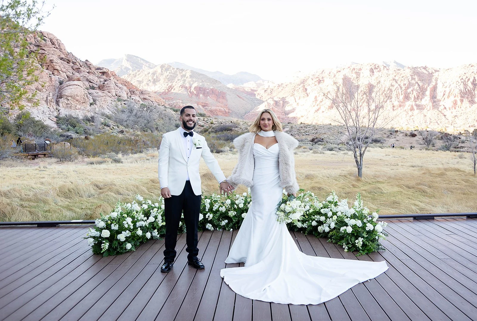 Full-length portrait of Melysa and Carlos holding hands on ceremony deck at Red Spring Boardwalk Las Vegas elopement with red rock canyon view, hair by Luci and makeup by Natalia for Amelia C & Co, photography by Onyx & Arrow