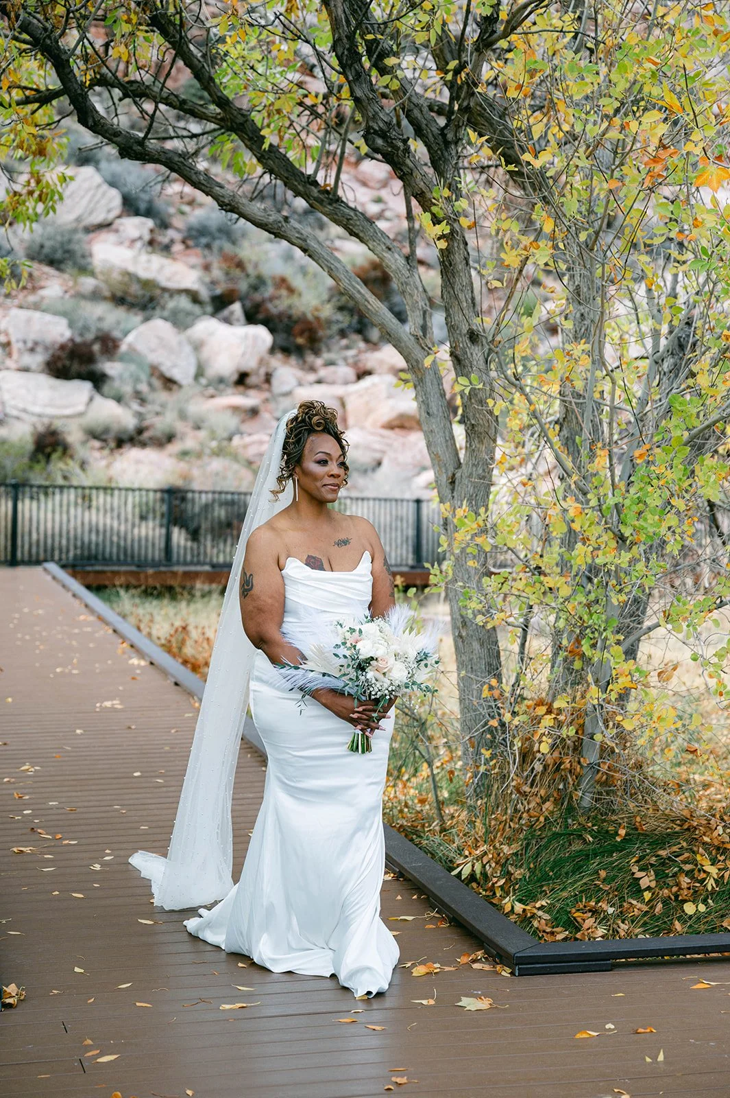 Bridal portrait of Aretha in strapless satin gown with pearl-edge veil and feather bouquet on boardwalk at Red Spring Boardwalk Las Vegas elopement in autumn, hair by Courtney and makeup by Natalia for Amelia C & Co, photography by Desert Wildflower
