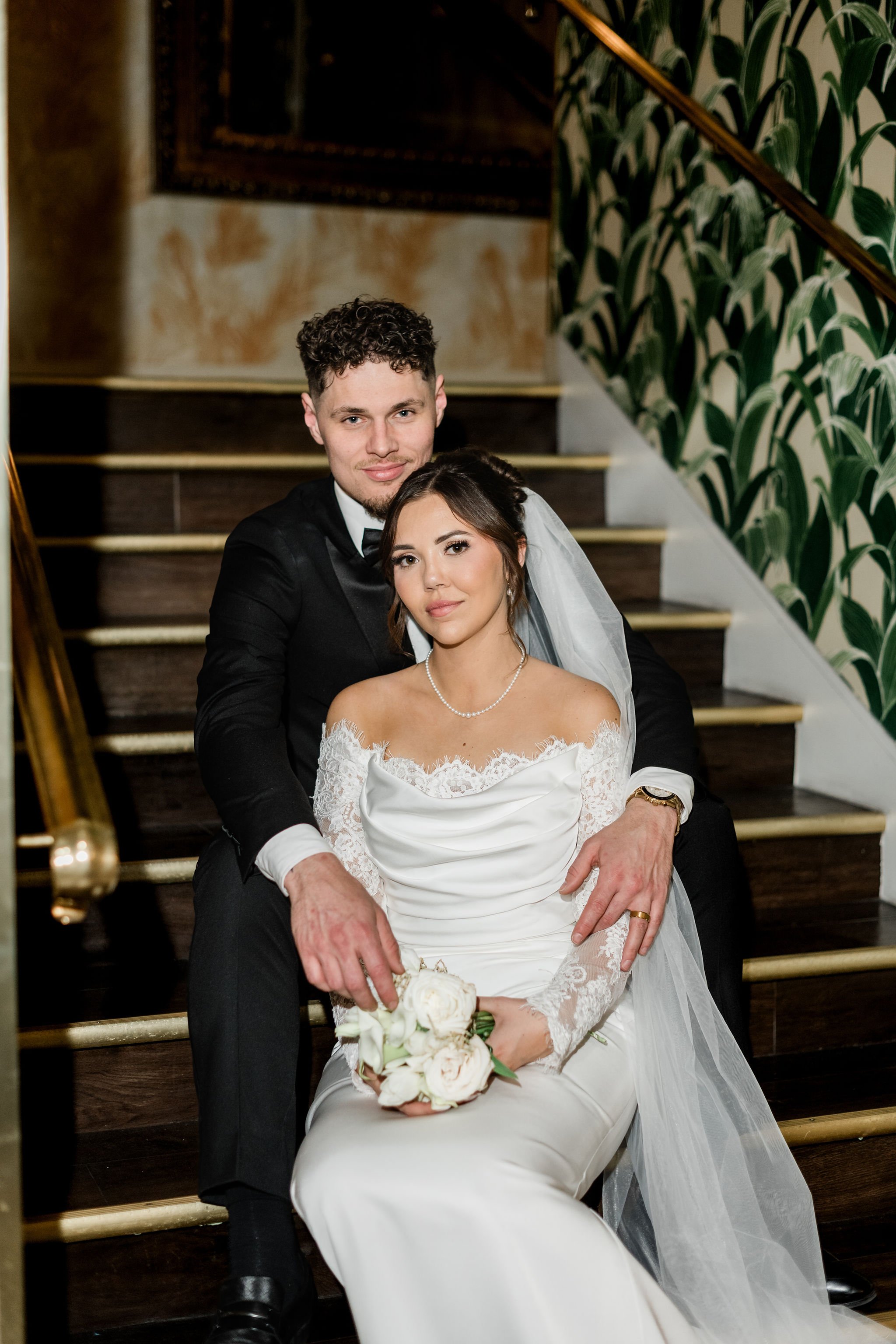 Bride Jessica and groom Lukas seated on ornate gold staircase at Hard Rock Hotel Las Vegas wedding, hair by Katie and makeup by Aimee for Amelia C & Co, photography by Liz Le