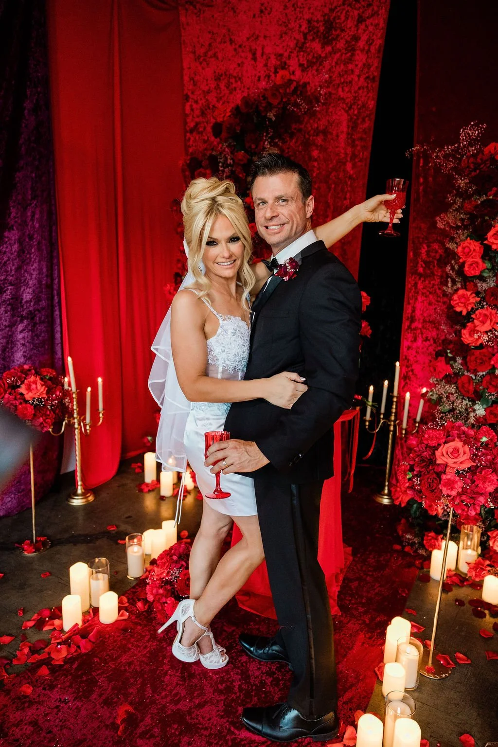 : Coby and Jacqueline toasting with red champagne glasses surrounded by candles and rose petals at Valentine's Day wedding Las Vegas, hair by Katie and makeup by Estefi for Amelia C & Co, photography by Liz Le