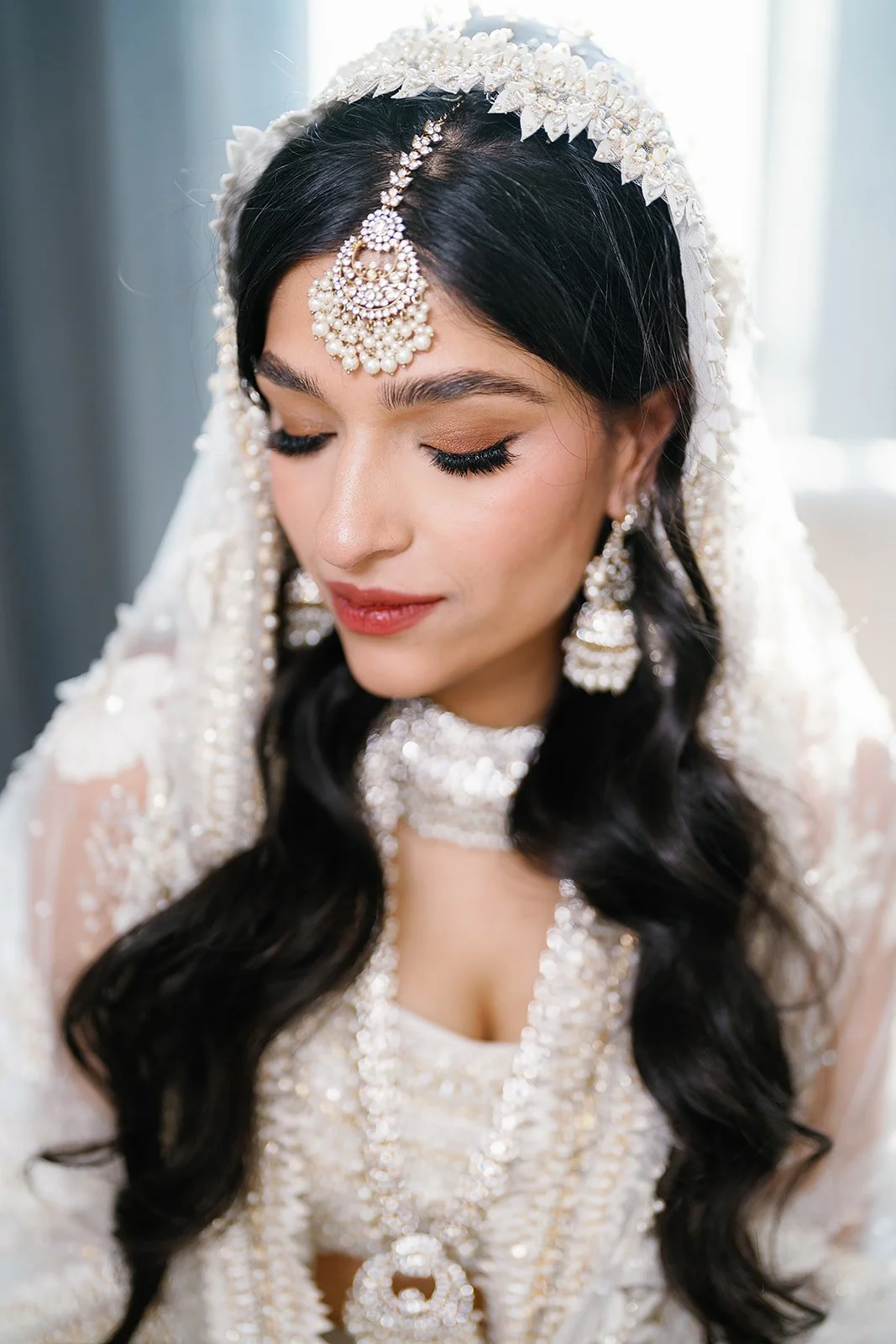 Full bridal portrait of Trusha seated in white lehenga with dupatta and gold jewelry at JW Marriott Las Vegas wedding, hair by Courtney and makeup by Natalia for Amelia C & Co, photography by Chernogorov Photography
