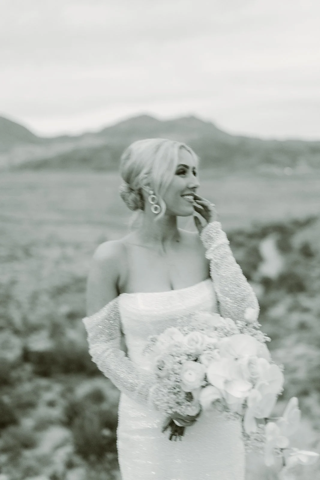 Black and white film style bridal portrait at Red Rock Canyon Las Vegas elopement, bride laughing with bouquet and desert mountain backdrop, hair and makeup by Luci L for Amelia C & Co, photography by Kristen Joy