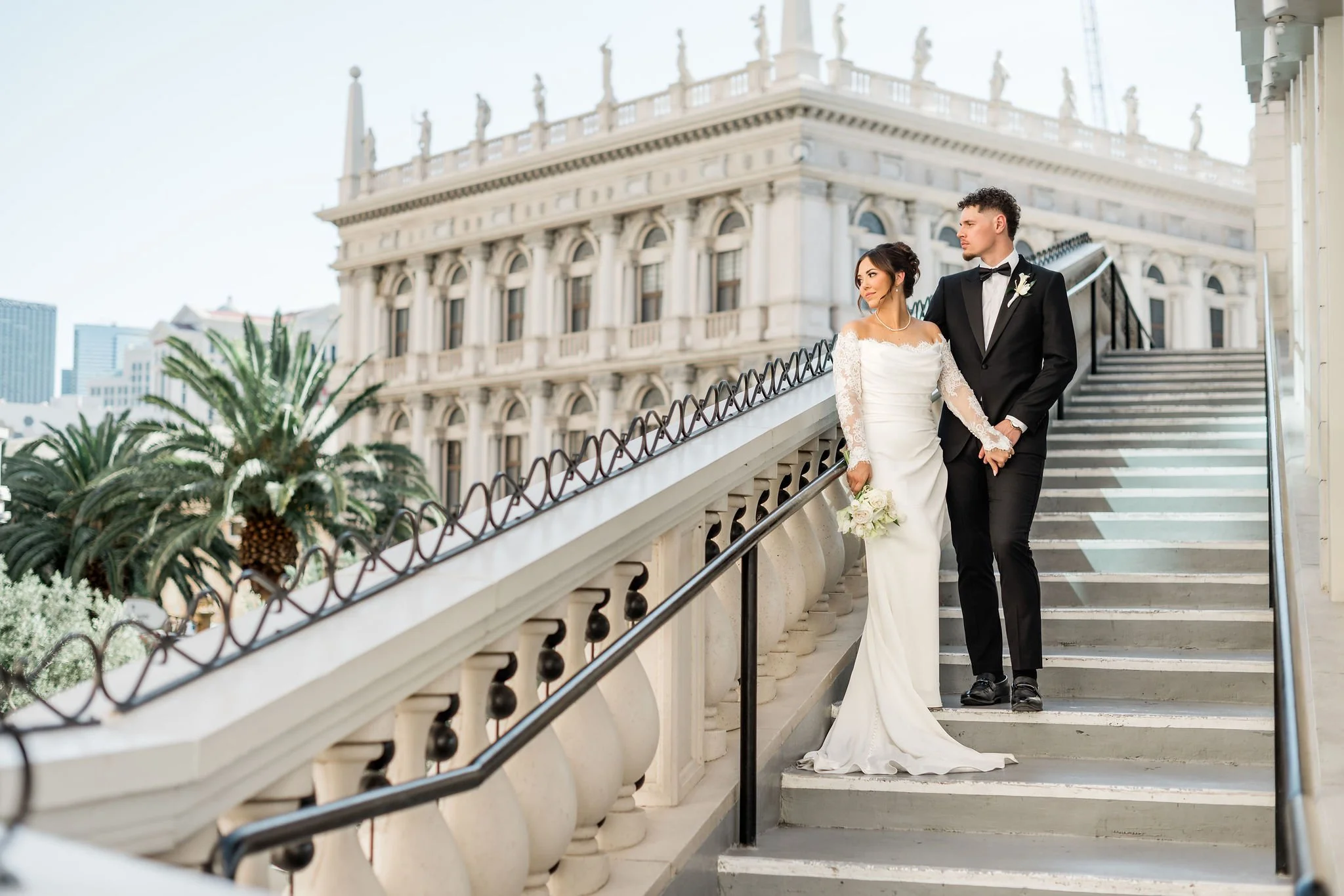 Bride Jessica and groom Lukas on grand exterior staircase at The Venetian Las Vegas with city skyline behind them, hair by Katie and makeup by Aimee for Amelia C & Co, photography by Liz Le