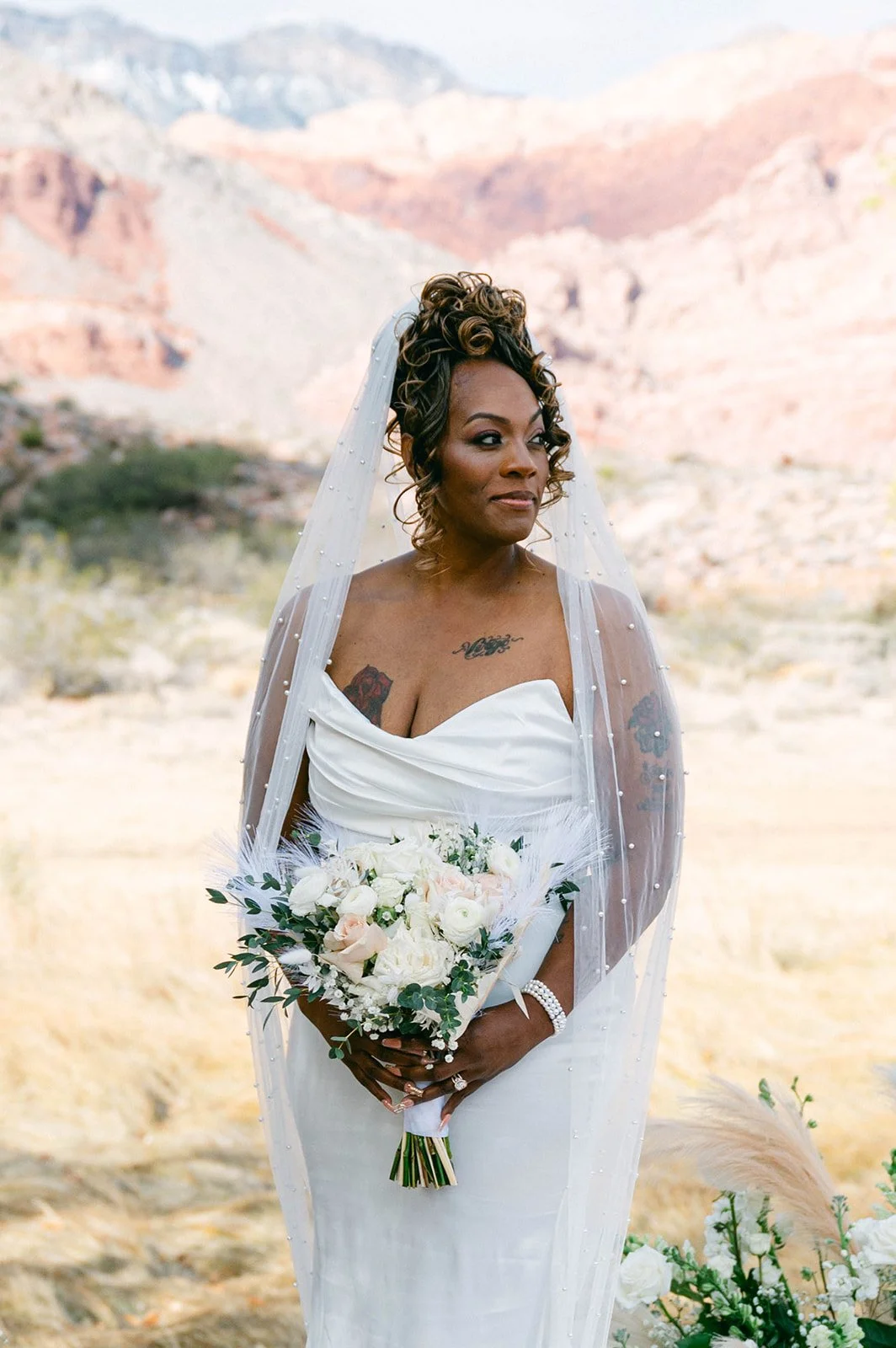 Bridal beauty portrait of Aretha with pearl veil curly updo and feather blush rose bouquet at Red Spring Boardwalk Las Vegas elopement, hair by Courtney and makeup by Natalia for Amelia C & Co, photography by Desert Wildflower