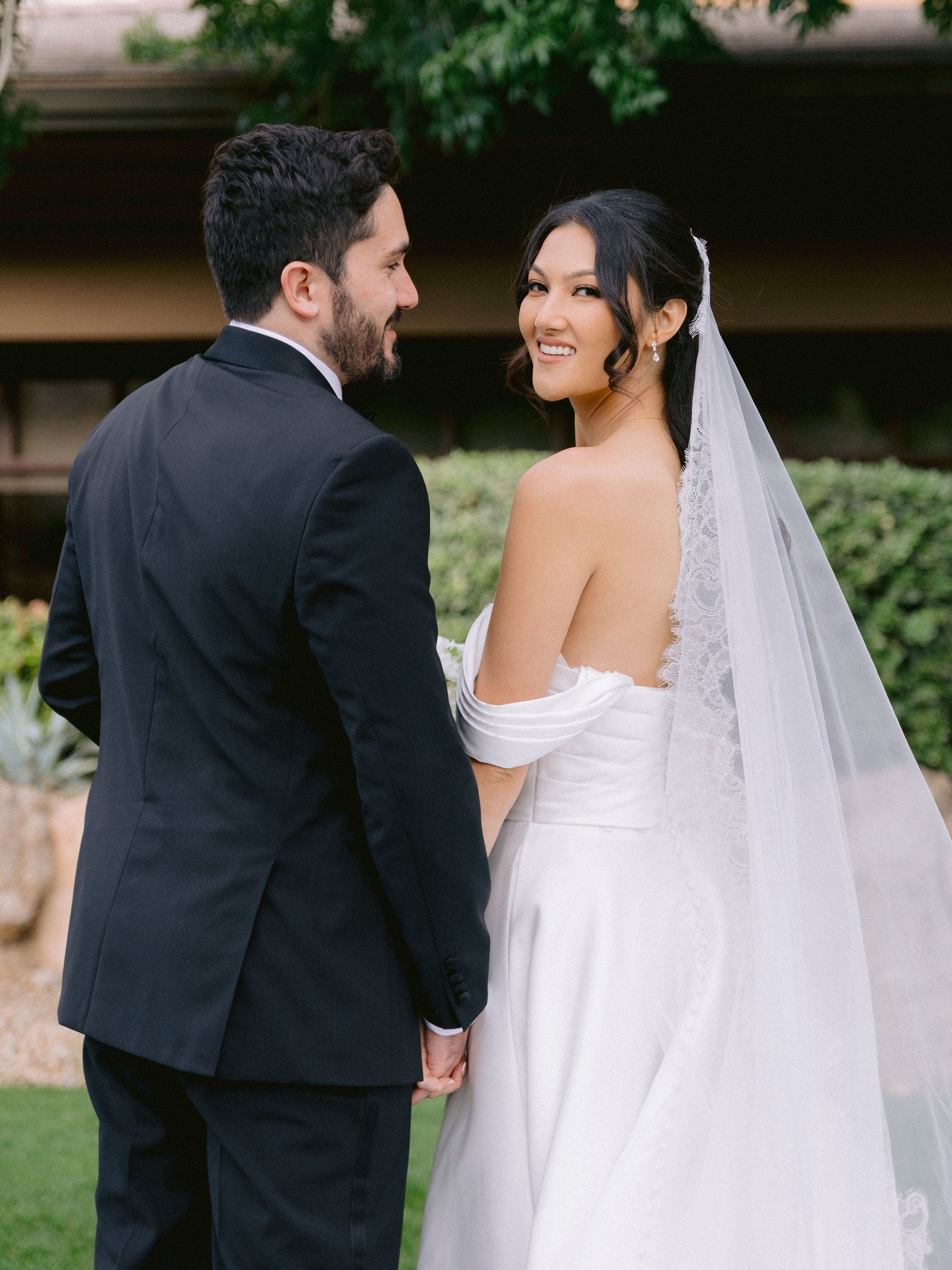 Bride looking back over shoulder at Las Vegas Paiute Golf Resort wedding showing lace veil detail and soft glam makeup, hair by Kari K and makeup by Natalia W for Amelia C & Co, photography by Susie and Will