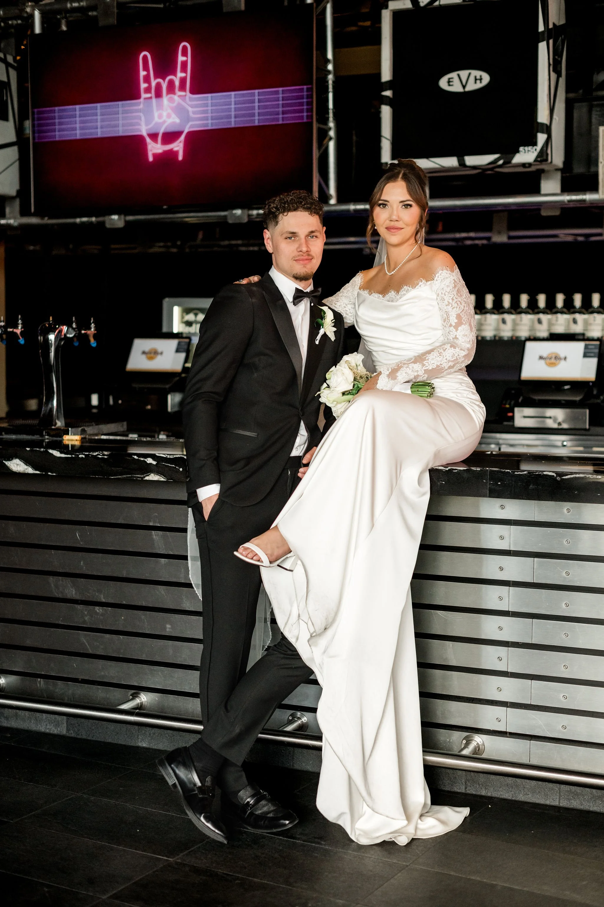 Bride Jessica sitting on bar with groom Lukas at Hard Rock Hotel Las Vegas wedding, hair by Katie and makeup by Aimee for Amelia C & Co, photography by Liz Le