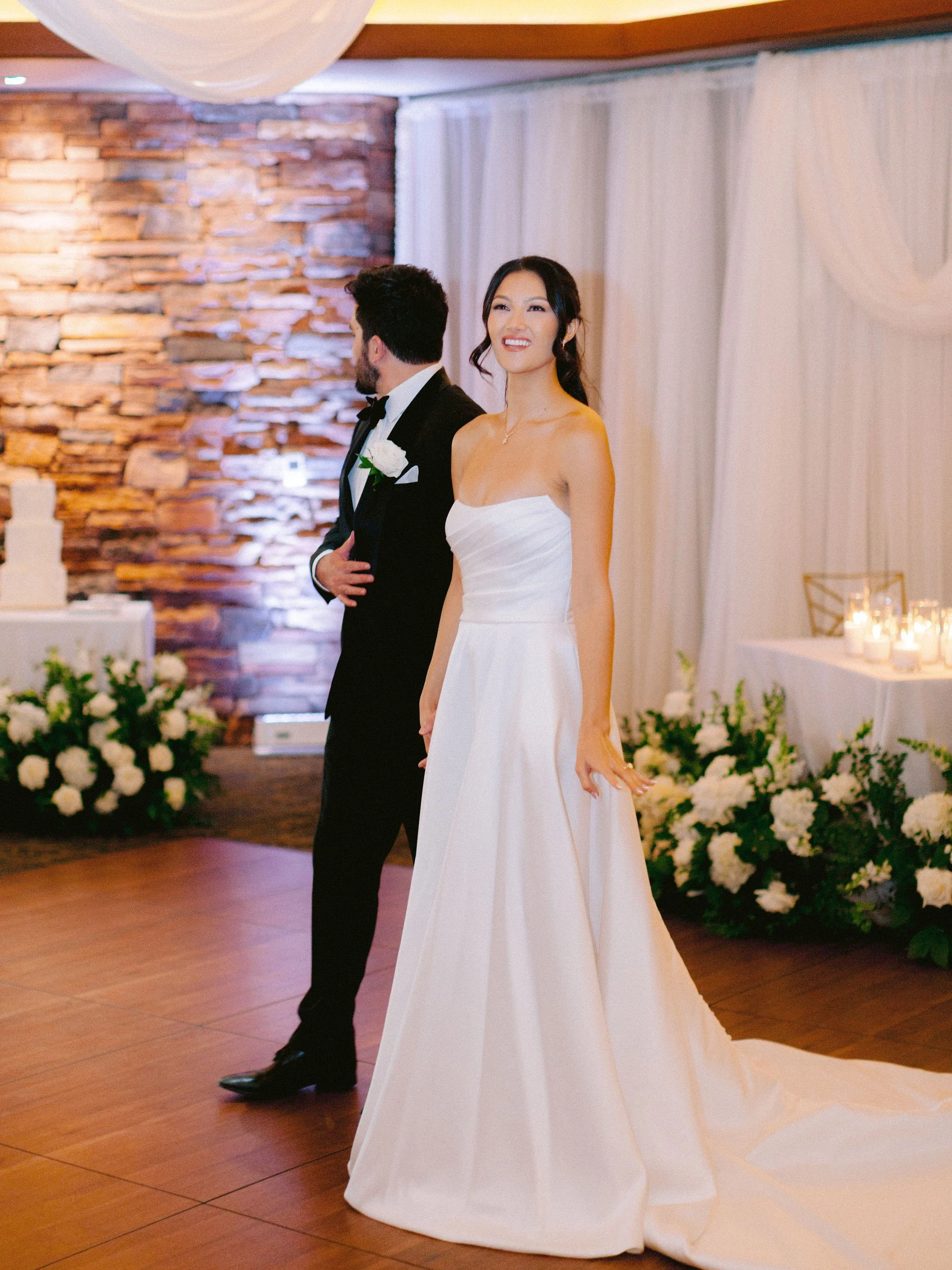 Bride during first dance at Las Vegas Paiute Golf Resort wedding reception with second look half updo and stone wall backdrop, hair by Kari K and makeup by Natalia W for Amelia C & Co, photography by Susie and Will