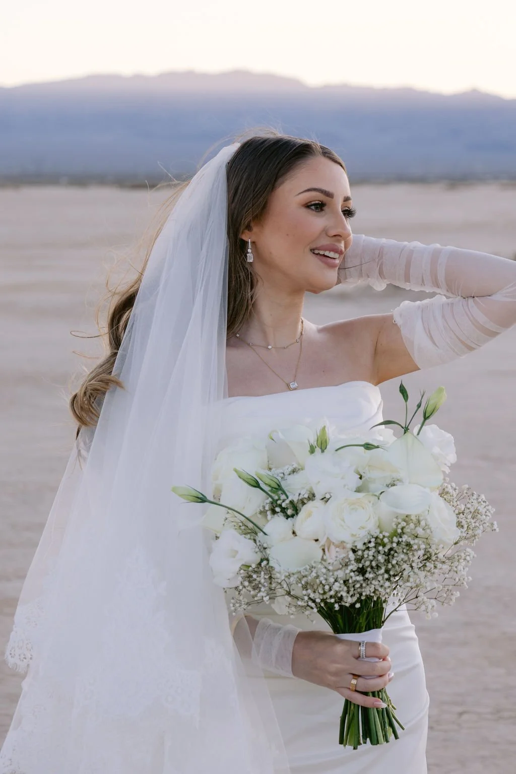 Cameron in veil and sheer sleeve gloves holding white bouquet at Dry Lake Bed Las Vegas elopement, hair and makeup by Marai for Amelia C & Co, photography by Sofia Teresa