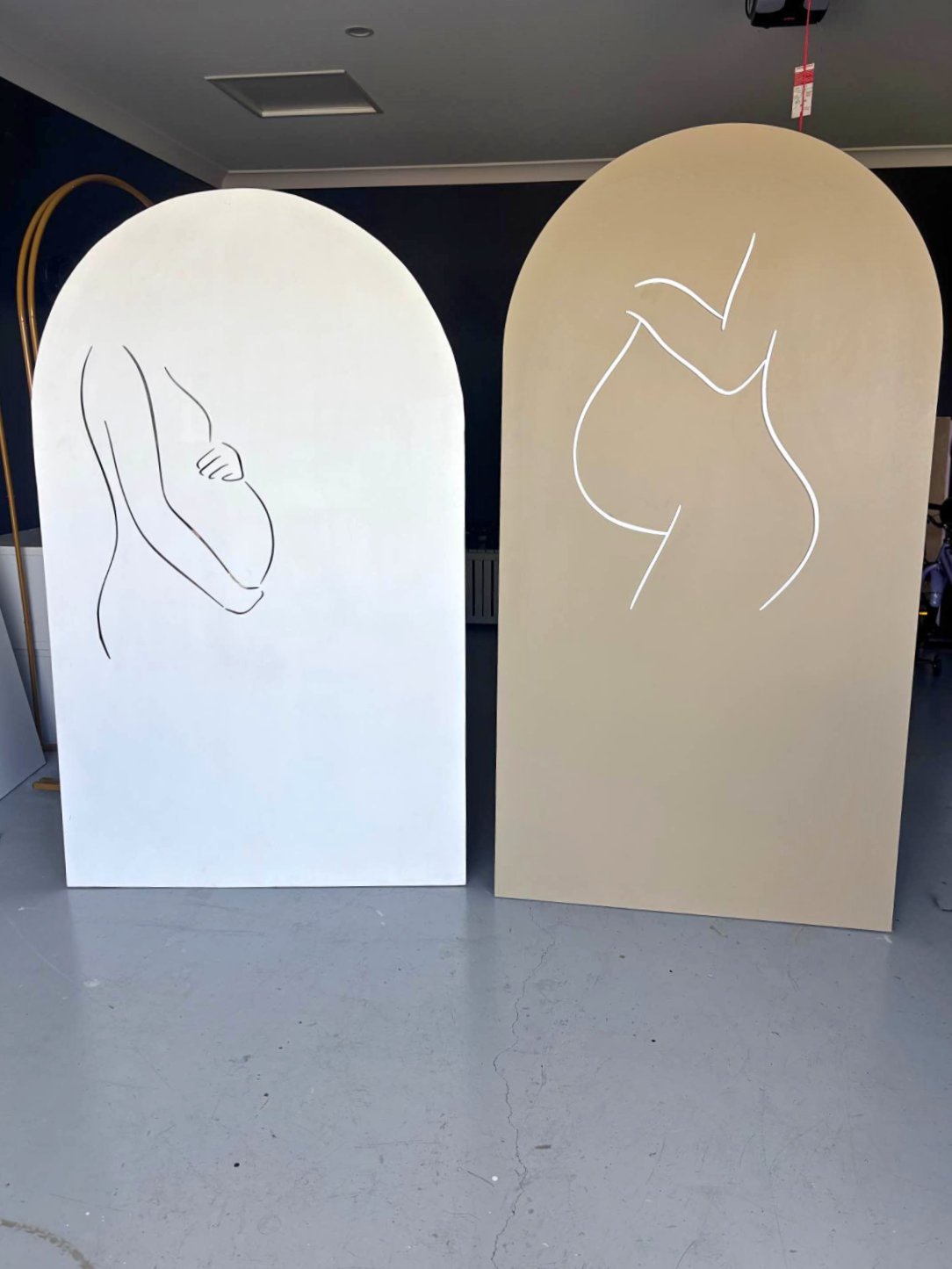 Two arched panels with minimalistic line drawings of female figures, one with crossed arms and the other with a curvy silhouette, set against an indoor background.