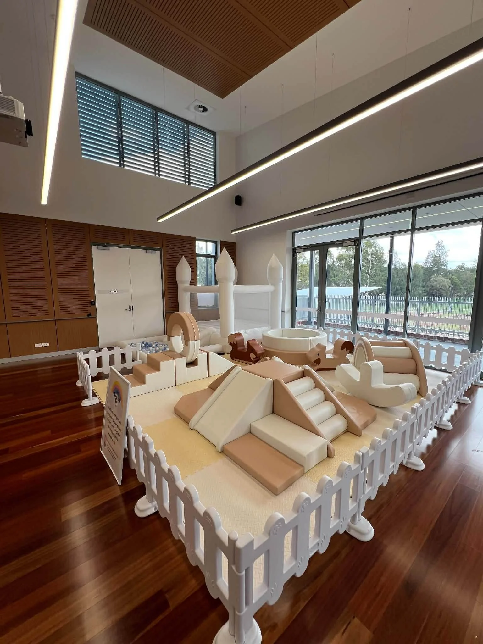 Indoor play area with soft foam slides and climbing structures inside a room with large windows, wooden paneling, and modern lighting.