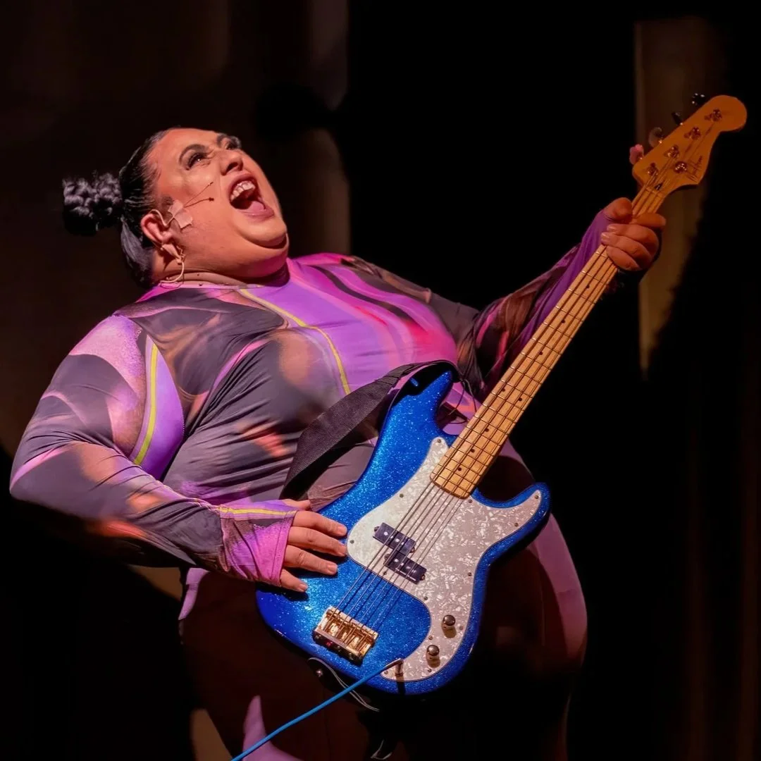 Performer passionately singing and playing a blue electric bass guitar on stage.