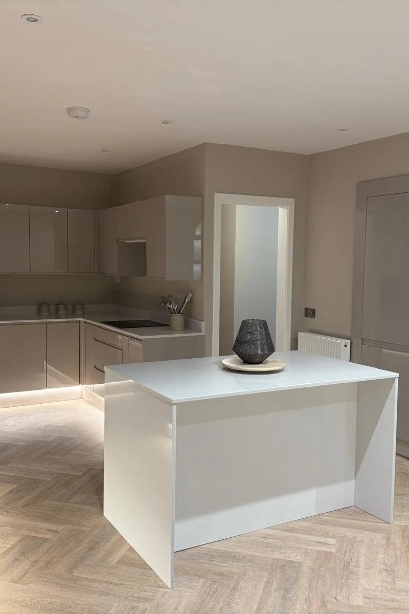 A modern kitchen with light-colored cabinets and a white kitchen island with a black decorative bowl on top.